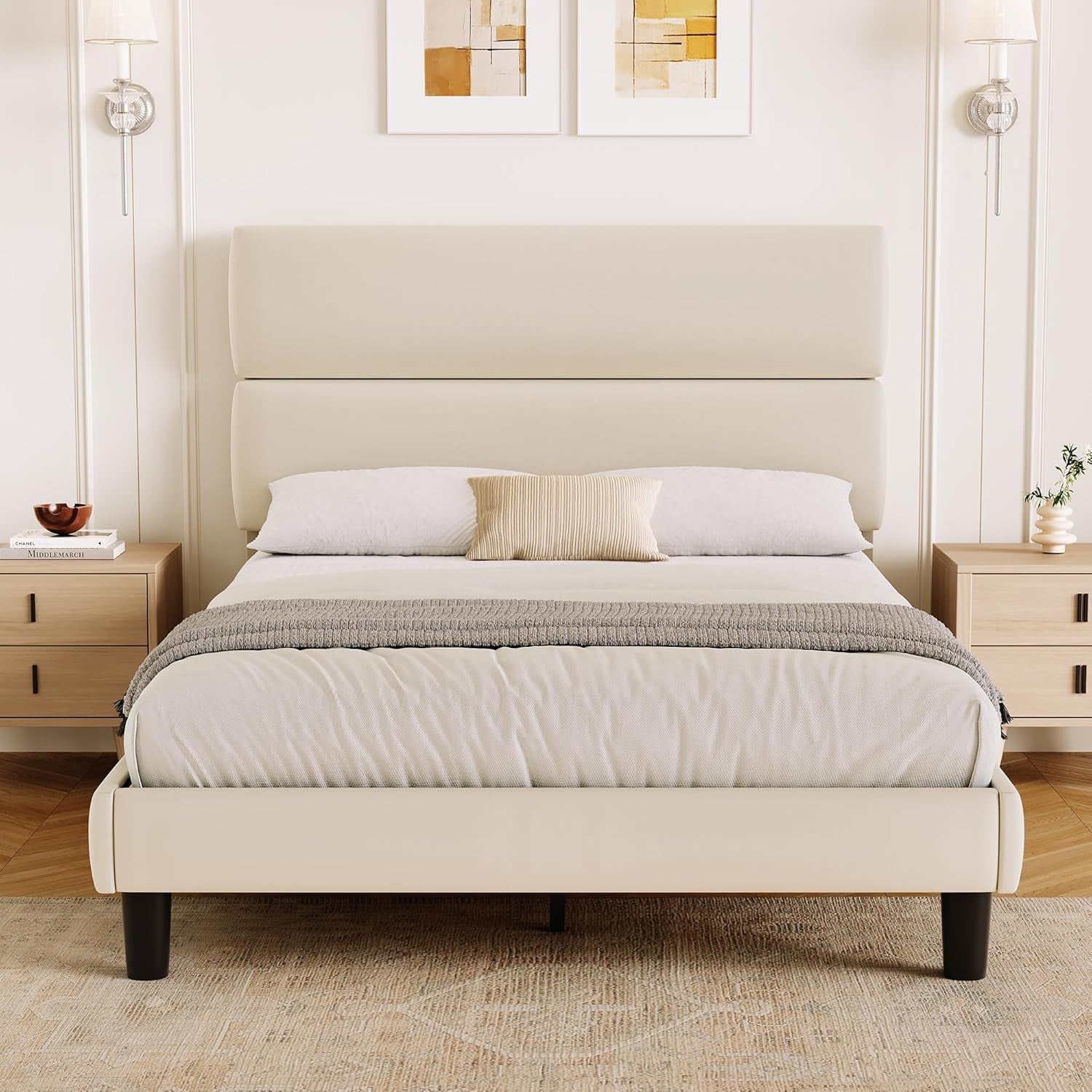 Front room view of a cream upholstered bed with a raised two-section headboard and black legs.