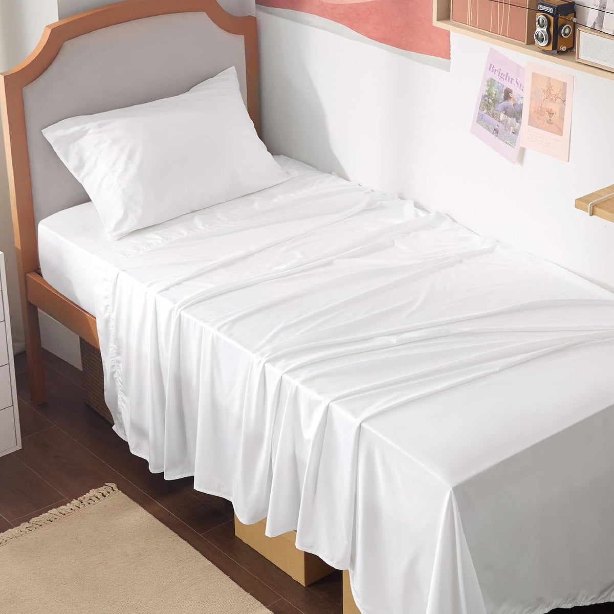 White sheets and a pillow on a single bed with a light wood frame and small wall decor.