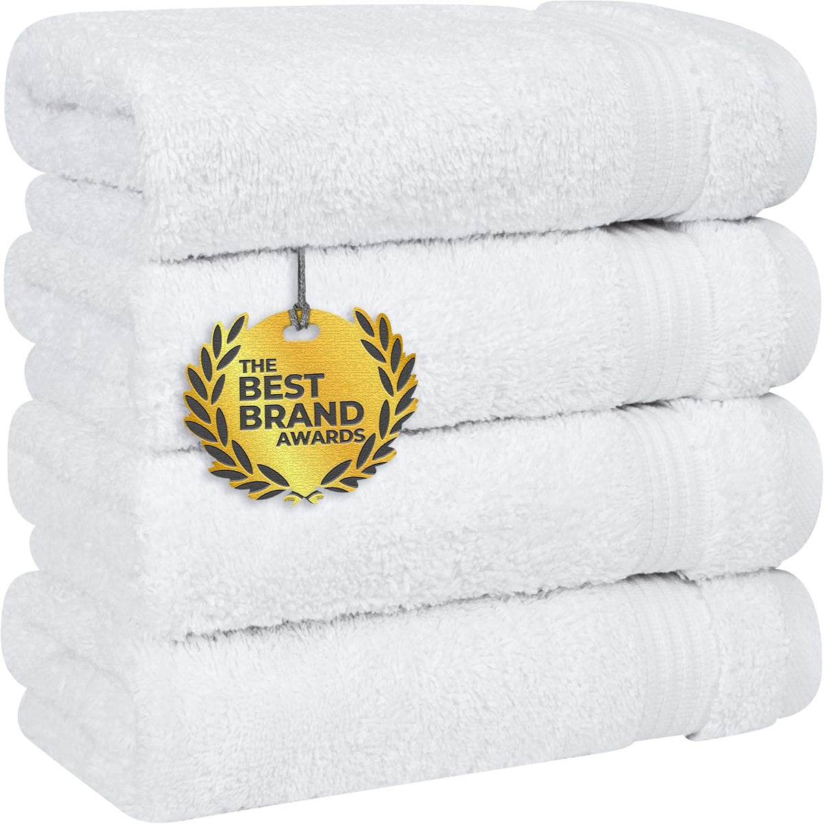 Low-angle close-up of four thick white towels stacked, showing plush pile, folded ends and a hanging gold medallion tag.
