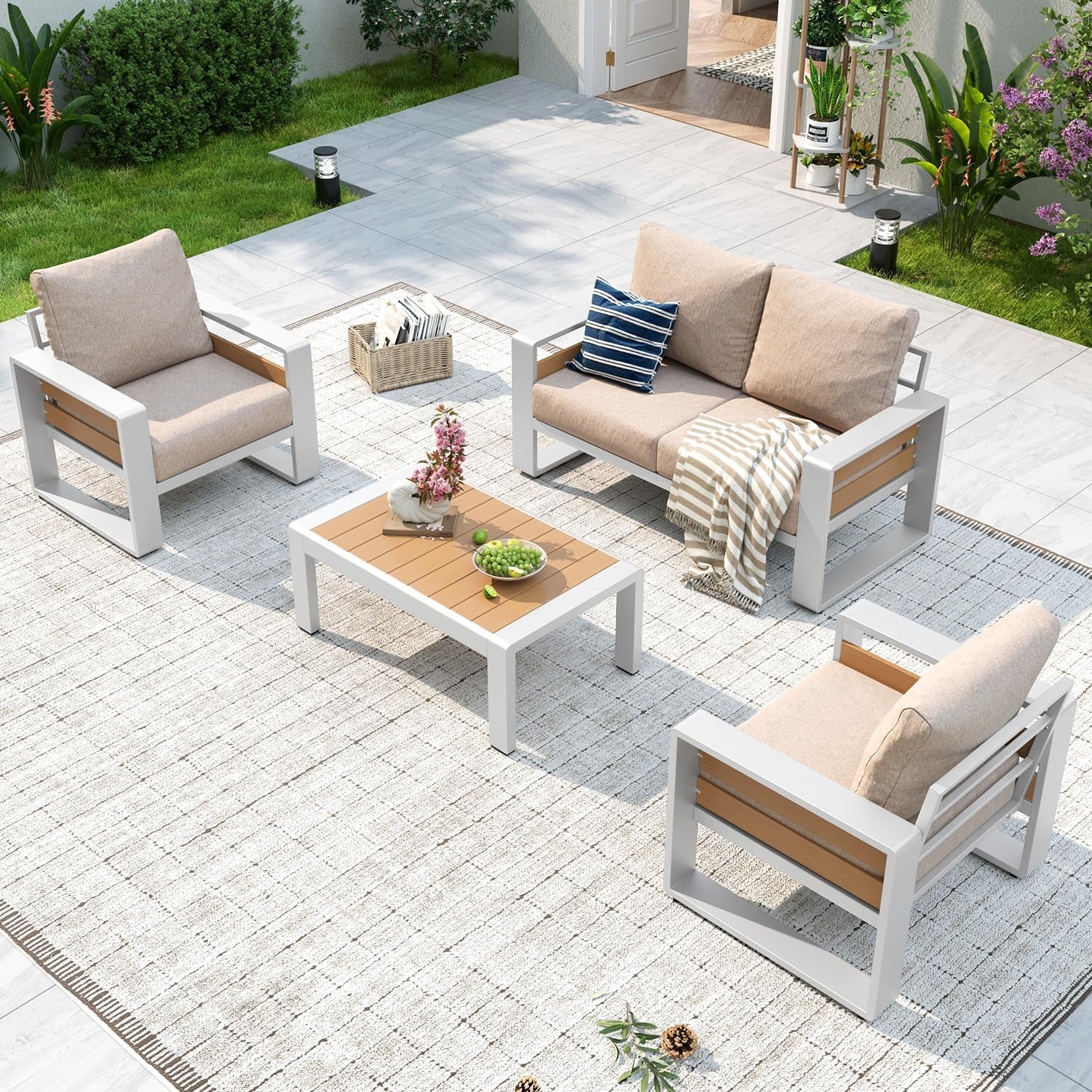 Overhead view of white-framed outdoor seating with beige cushions on a pale woven rug and tile patio.