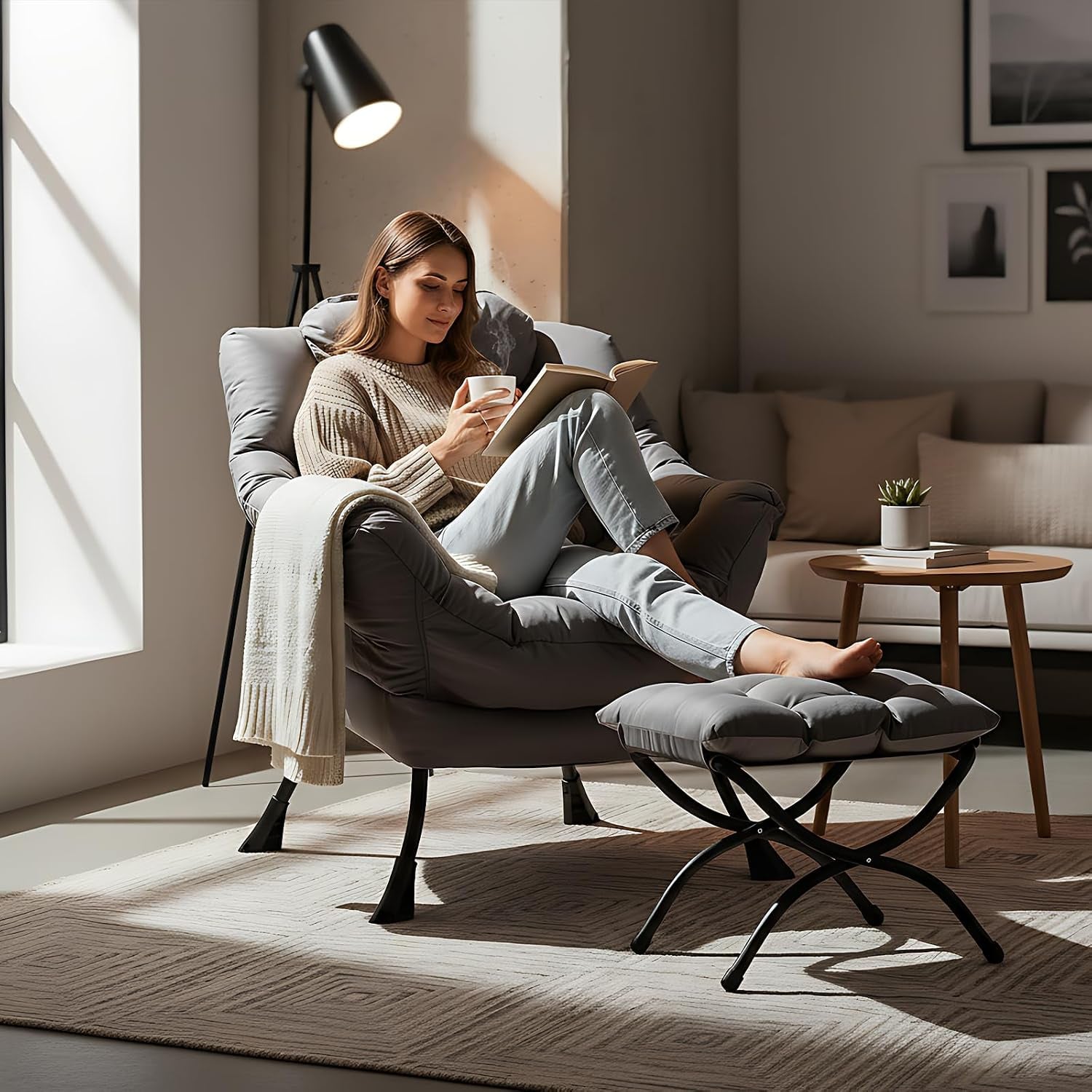 Woman reading in the dark grey lounge chair with ottoman by a floor lamp in a living room