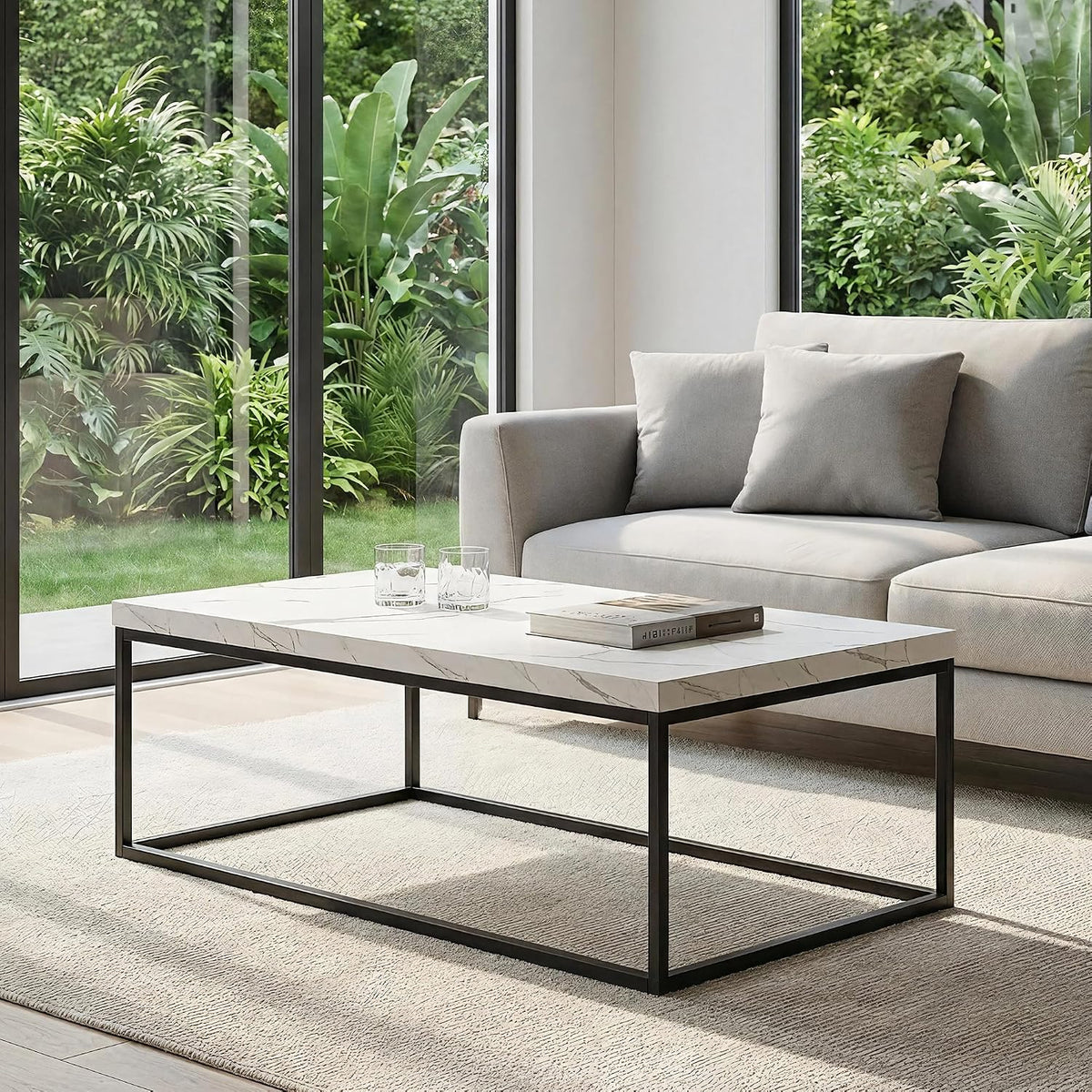 White marble top coffee table with black rectangular metal base shown in a bright room by large windows