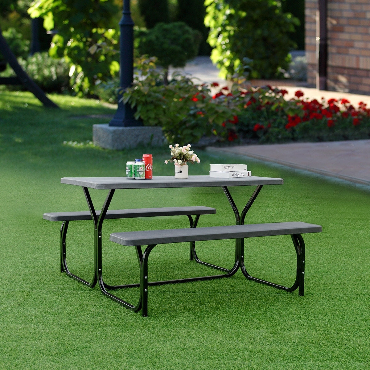 Picnic table set on grass beside a garden, with drinks, flowers, and a small box on the table.
