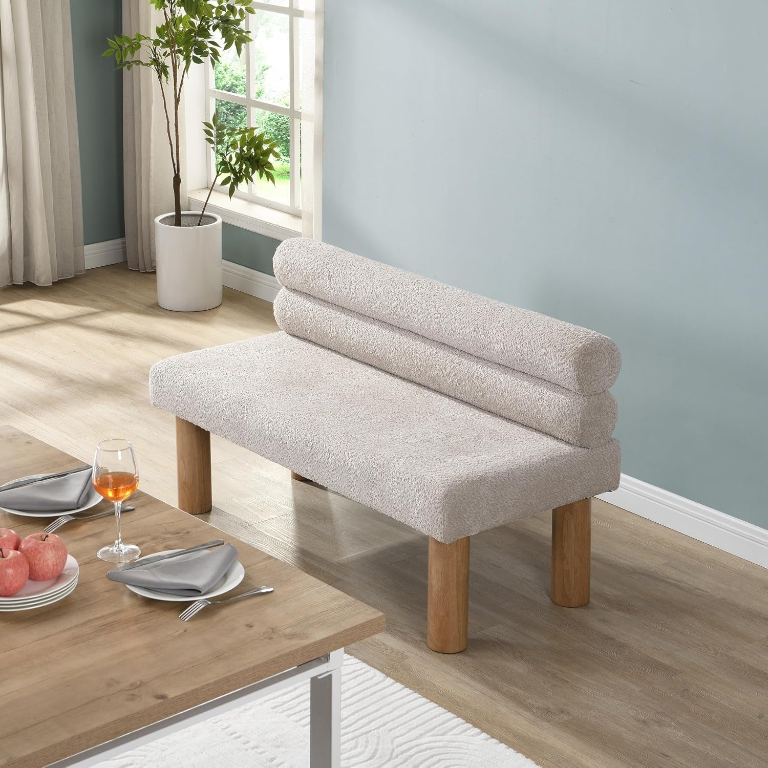 Light beige boucle bench placed next to a wooden dining table by a window, angled lifestyle view