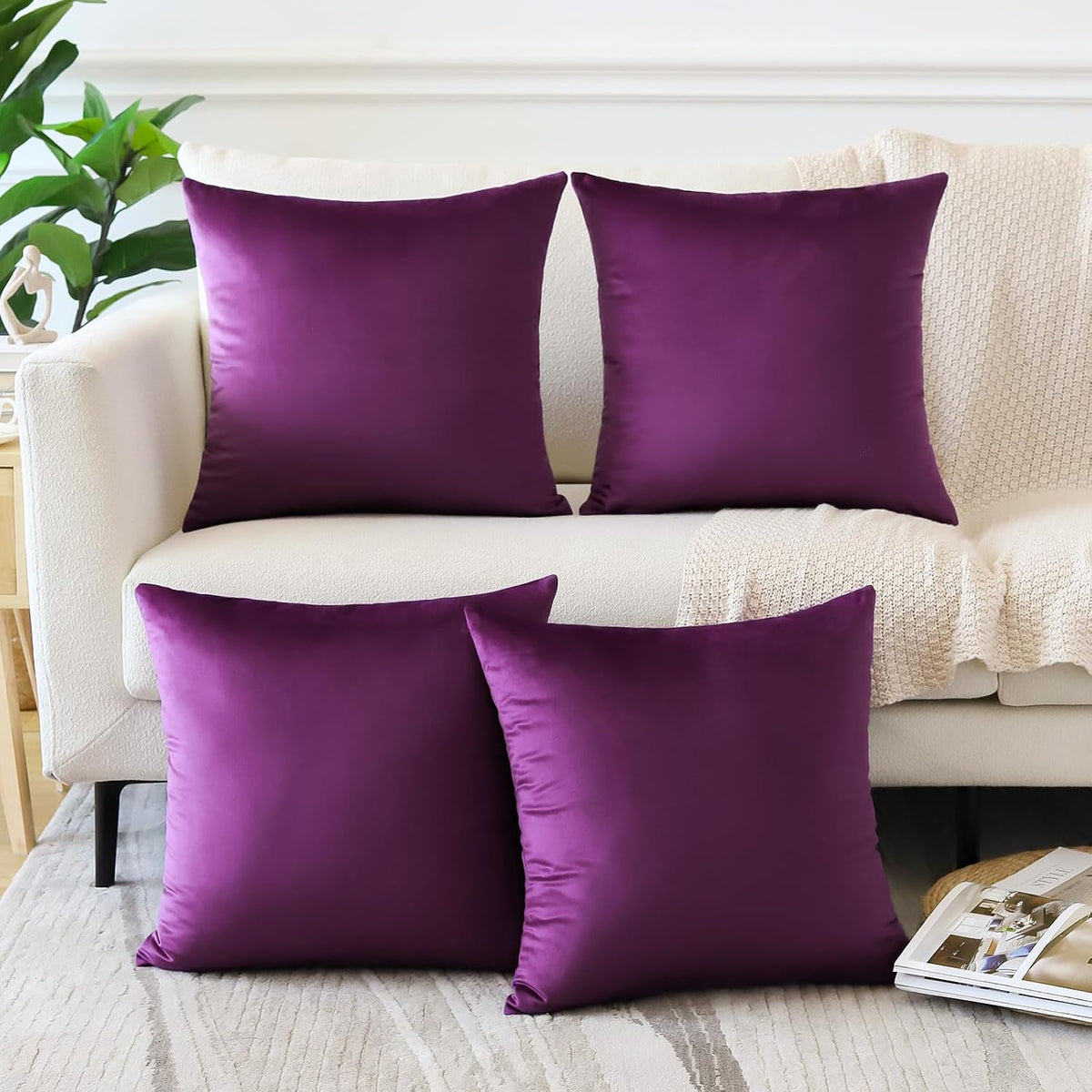 Four square velvet pillow covers in bright purple displayed on a cream sofa with a knit throw.
