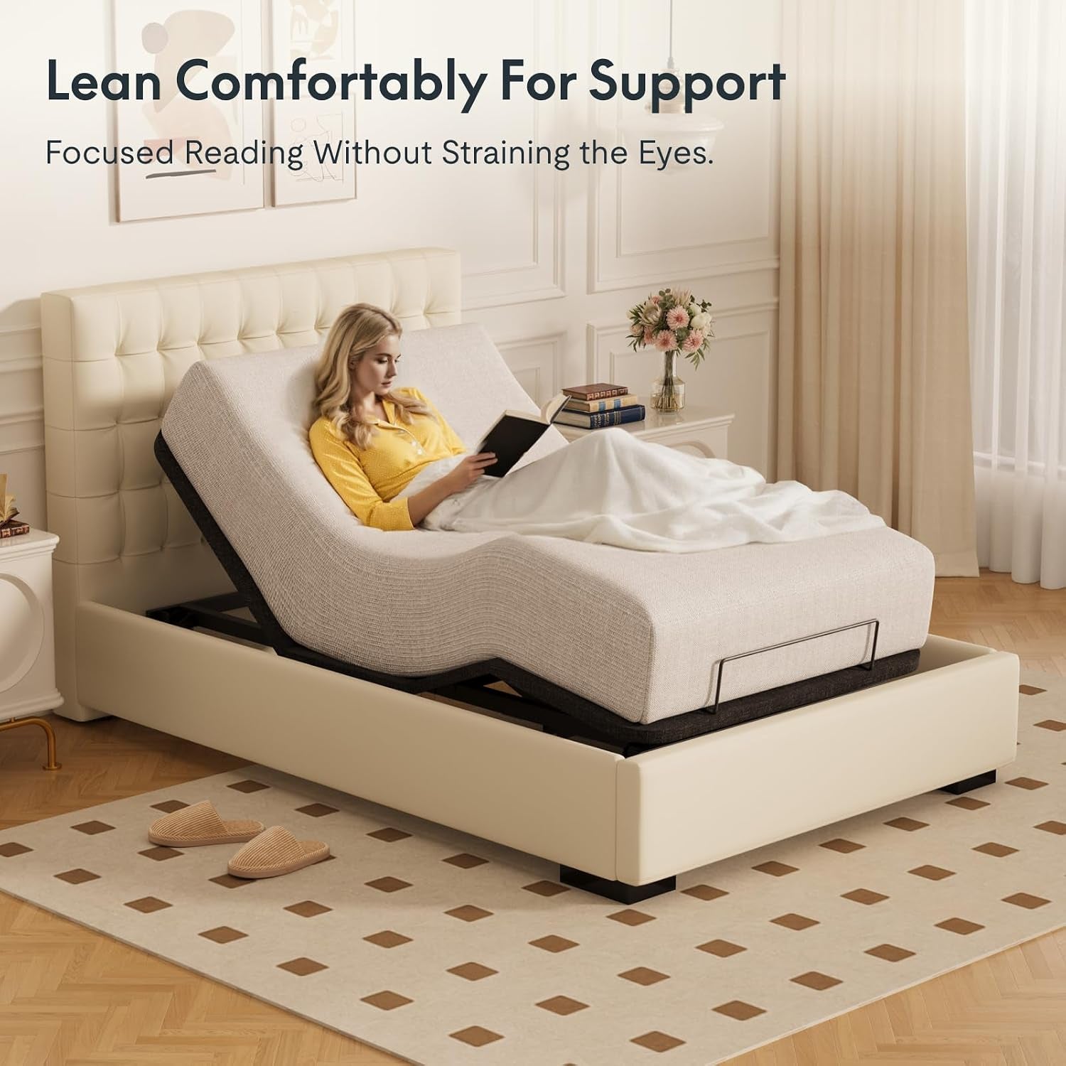 Beige upholstered bed in a bright bedroom; textured mattress curved, metal foot retainer and slippers on dotted rug visible.