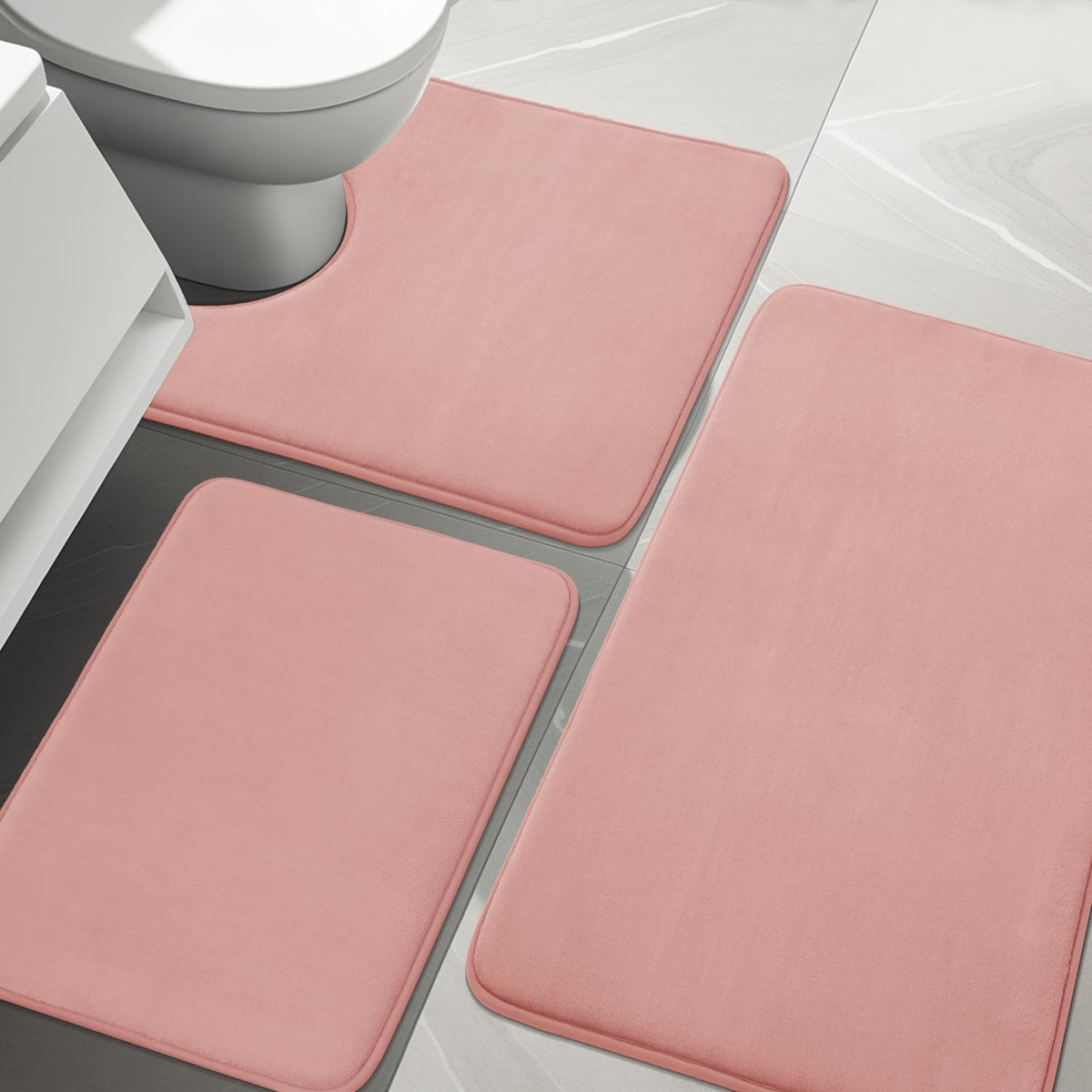 Top-down bathroom view showing three pink memory-foam rugs, one contoured around a toilet base.