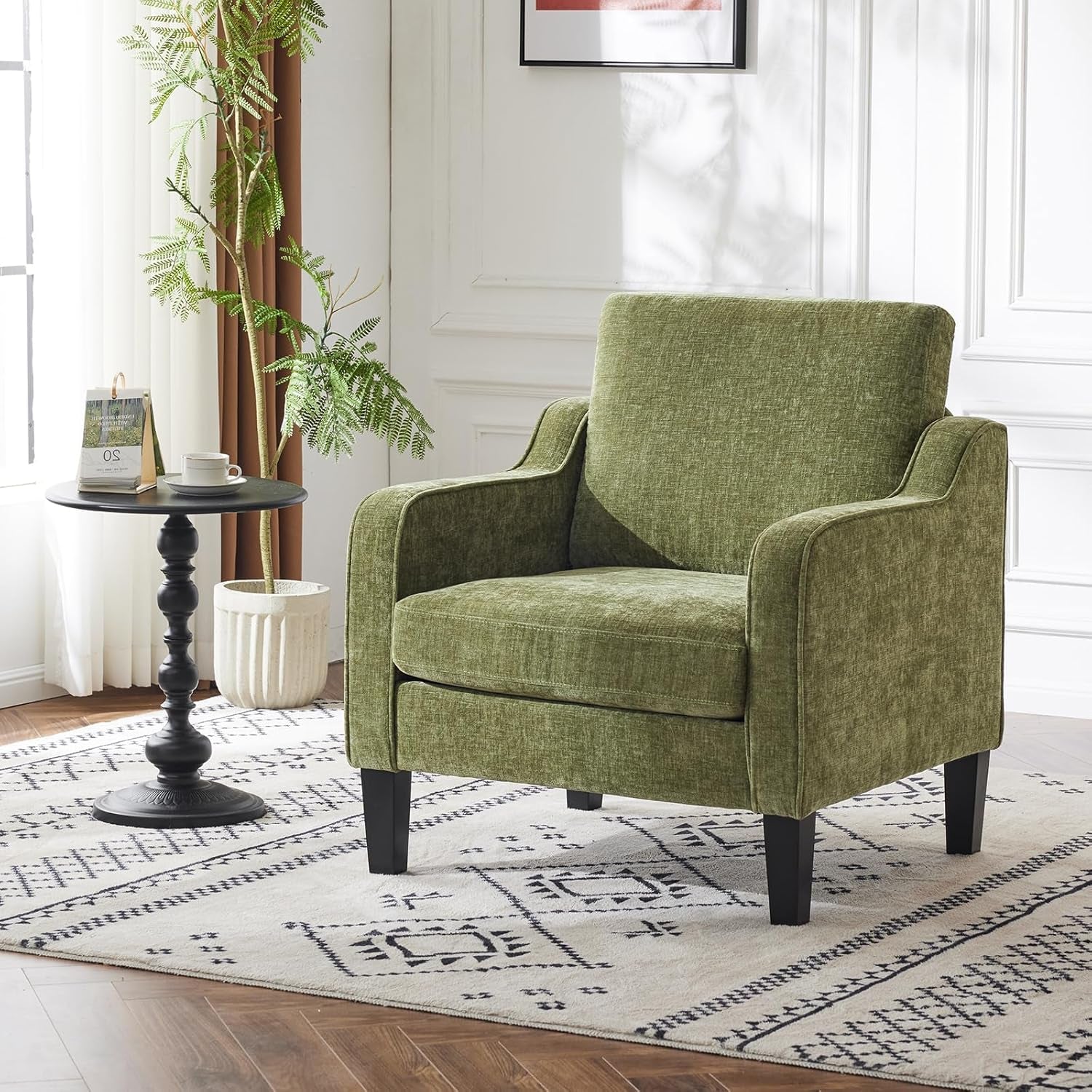 Green upholstered accent chair staged in a bright room on a patterned rug next to a round side table