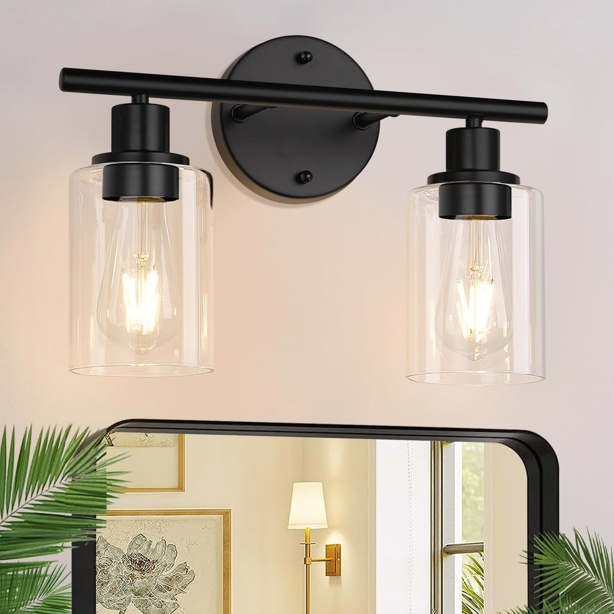 Close-up of a black two-light vanity fixture with clear cylindrical glass shades over a mirror.