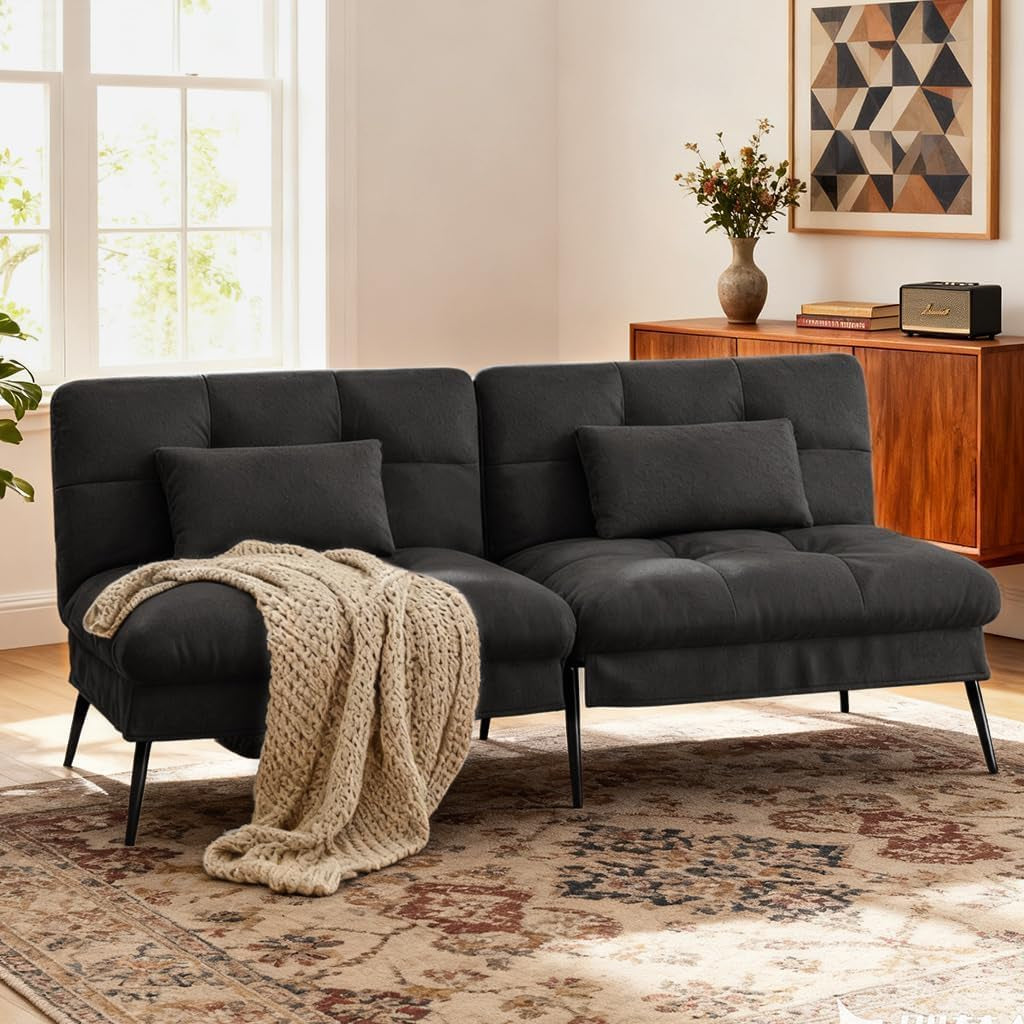 Black futon laid flat as a bed with throw blanket and two pillows in a bright room
