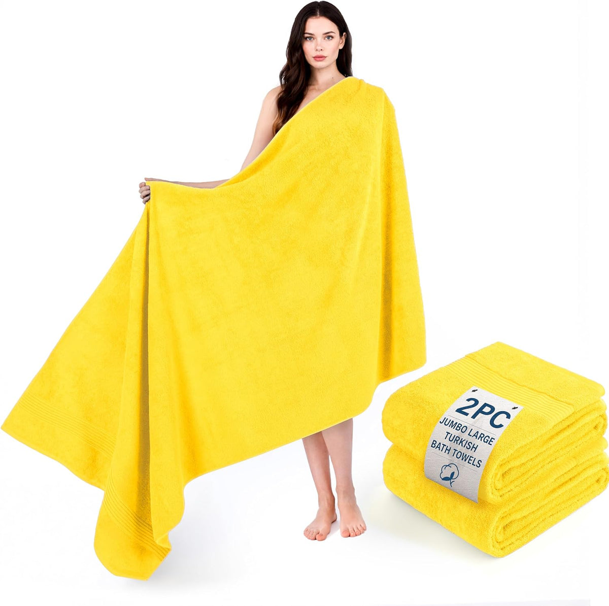 Woman draped in a large bright yellow bath towel holding it open with a folded towel stack beside her.