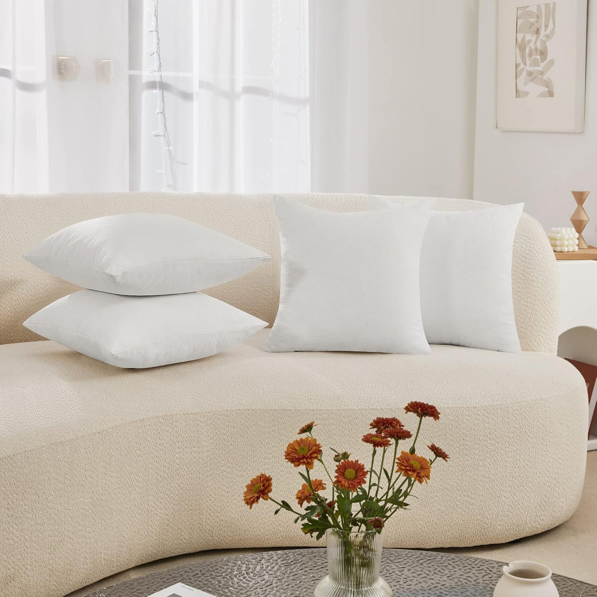 Two white pillow covers displayed on a cream boucle sofa with flowers on a table in front.