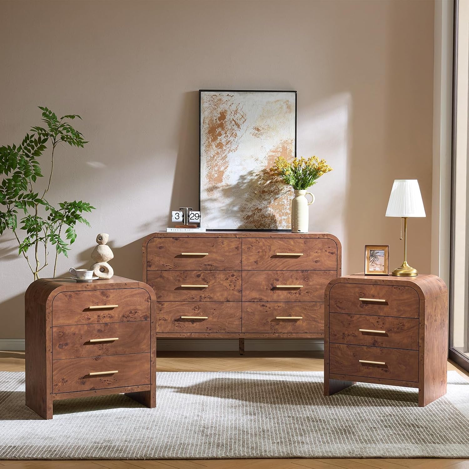 Brown dresser and nightstands styled with a tall potted plant and a lamp, sunlight casting shadows on the wall.