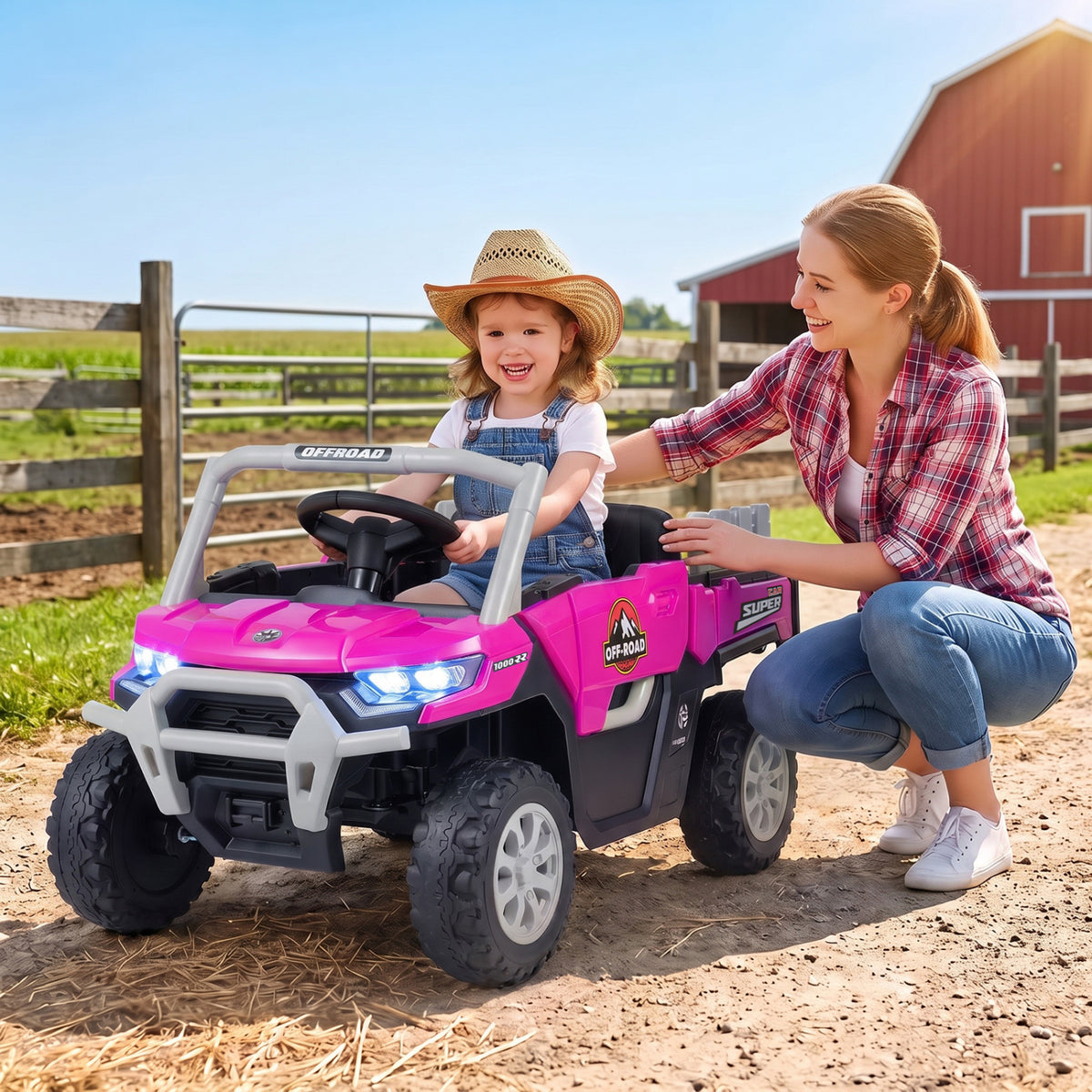 A child sits in a pink ride-on dump truck as an adult kneels beside it outdoors.