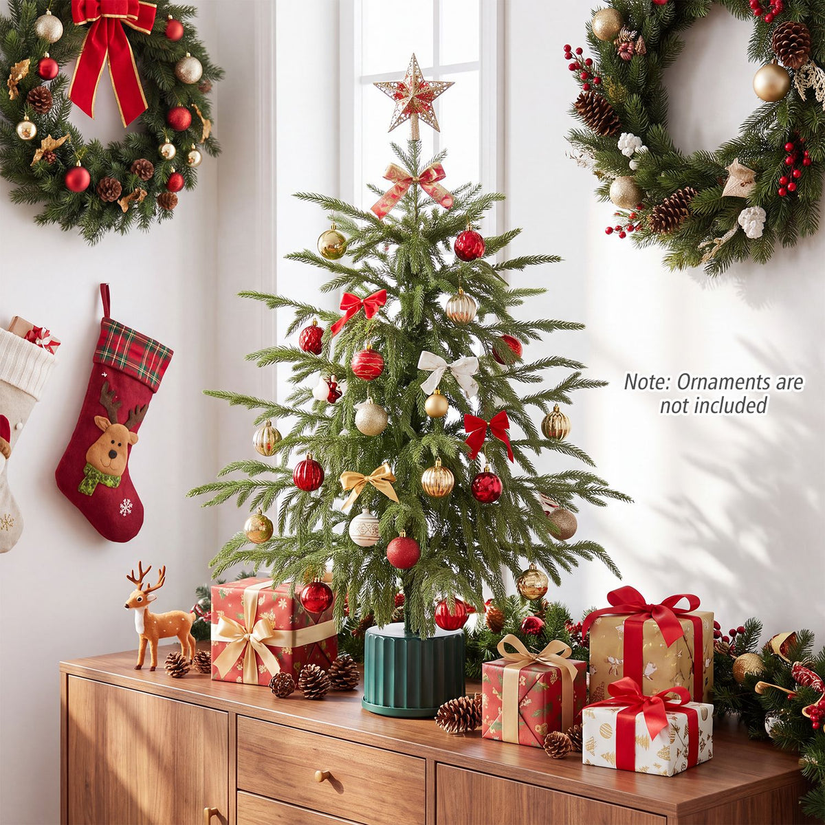 Decorated tabletop Christmas tree on a wooden cabinet, surrounded by gifts and holiday decor.