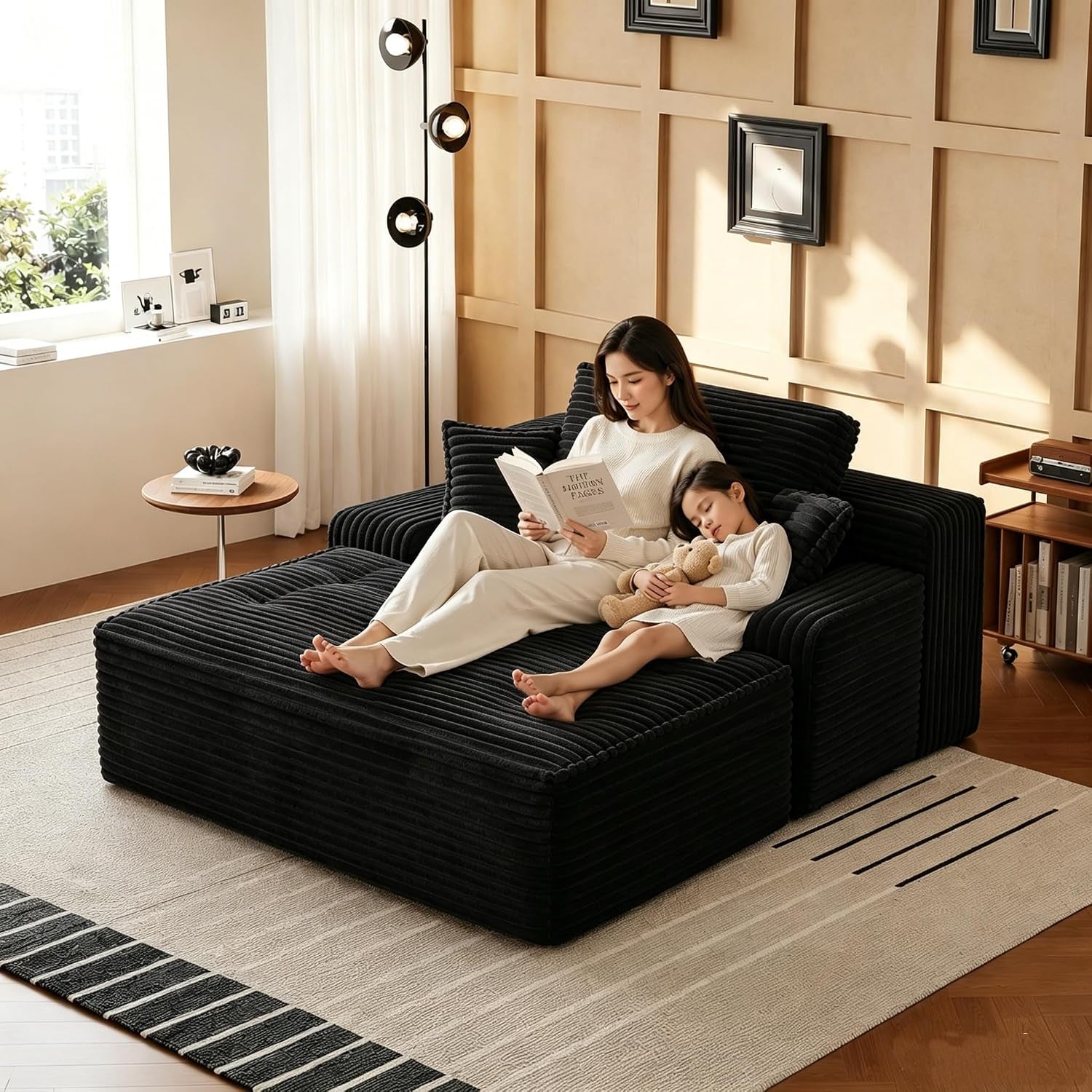 Black deep-seat chaise in a living room with a woman reading and a child asleep beside her.