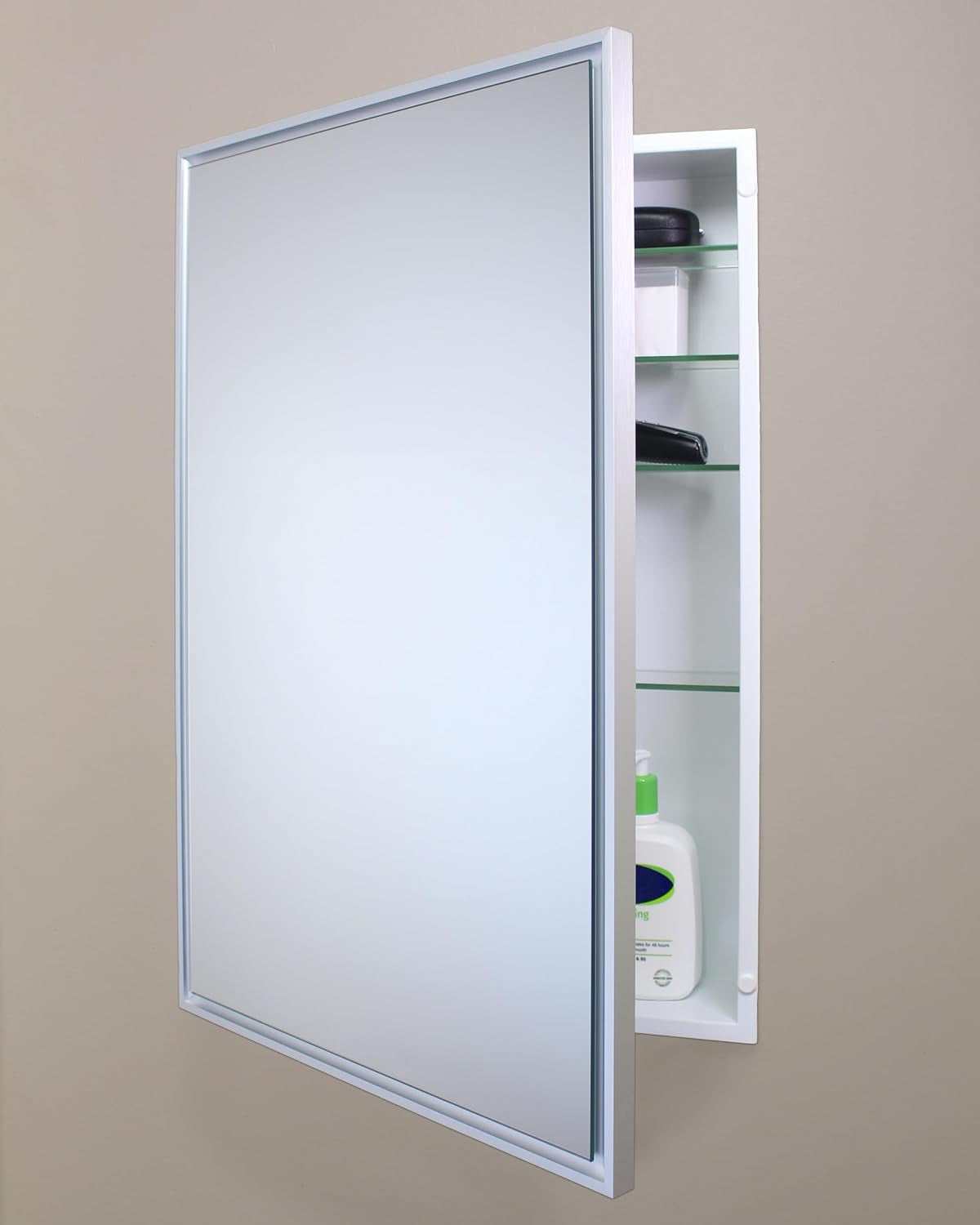 Silver-framed recessed medicine cabinet mounted on beige wall, door open showing bottle on lower shelf