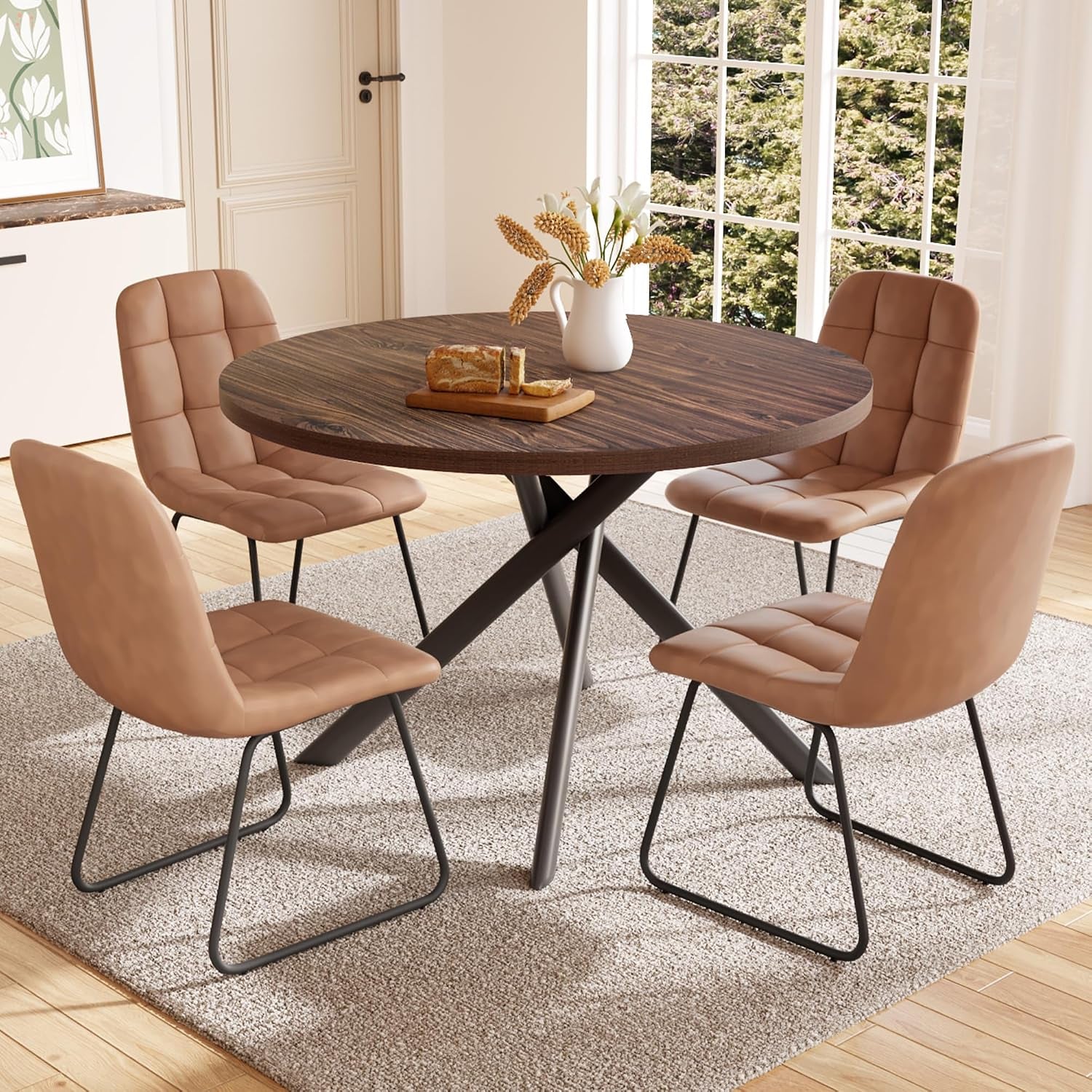 Round dark-walnut table surrounded by four tan upholstered U-shaped chairs in a bright room