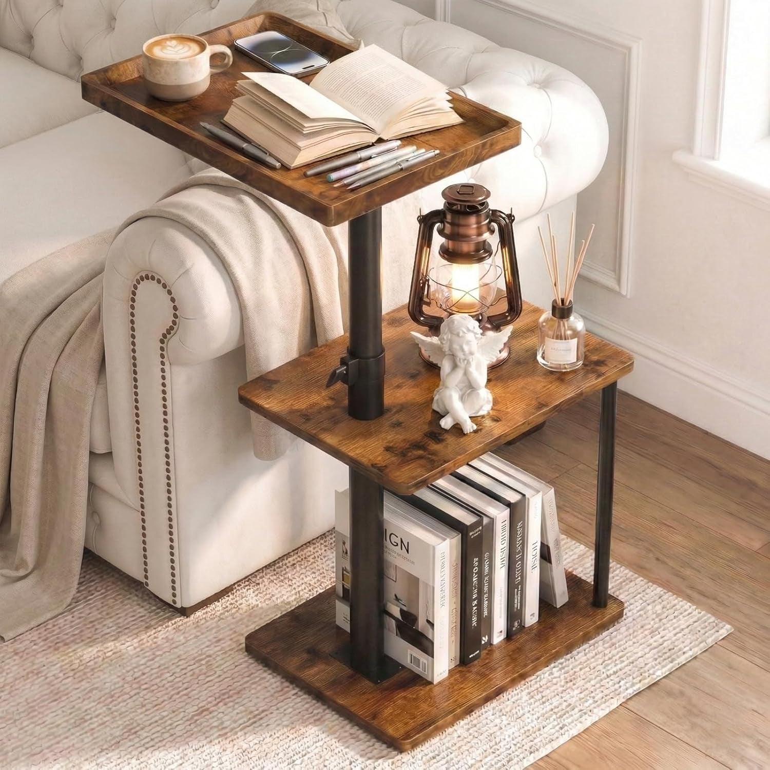 Close side view of a rectangular three-tier C‑shaped table next to a tufted white sofa with books, a lantern and small decor.