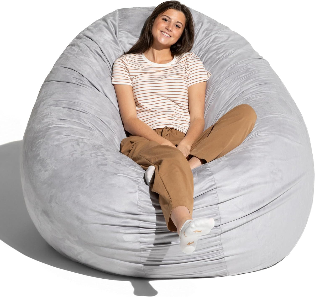 Woman seated inside a light gray oversized bean bag chair, leaning back and smiling