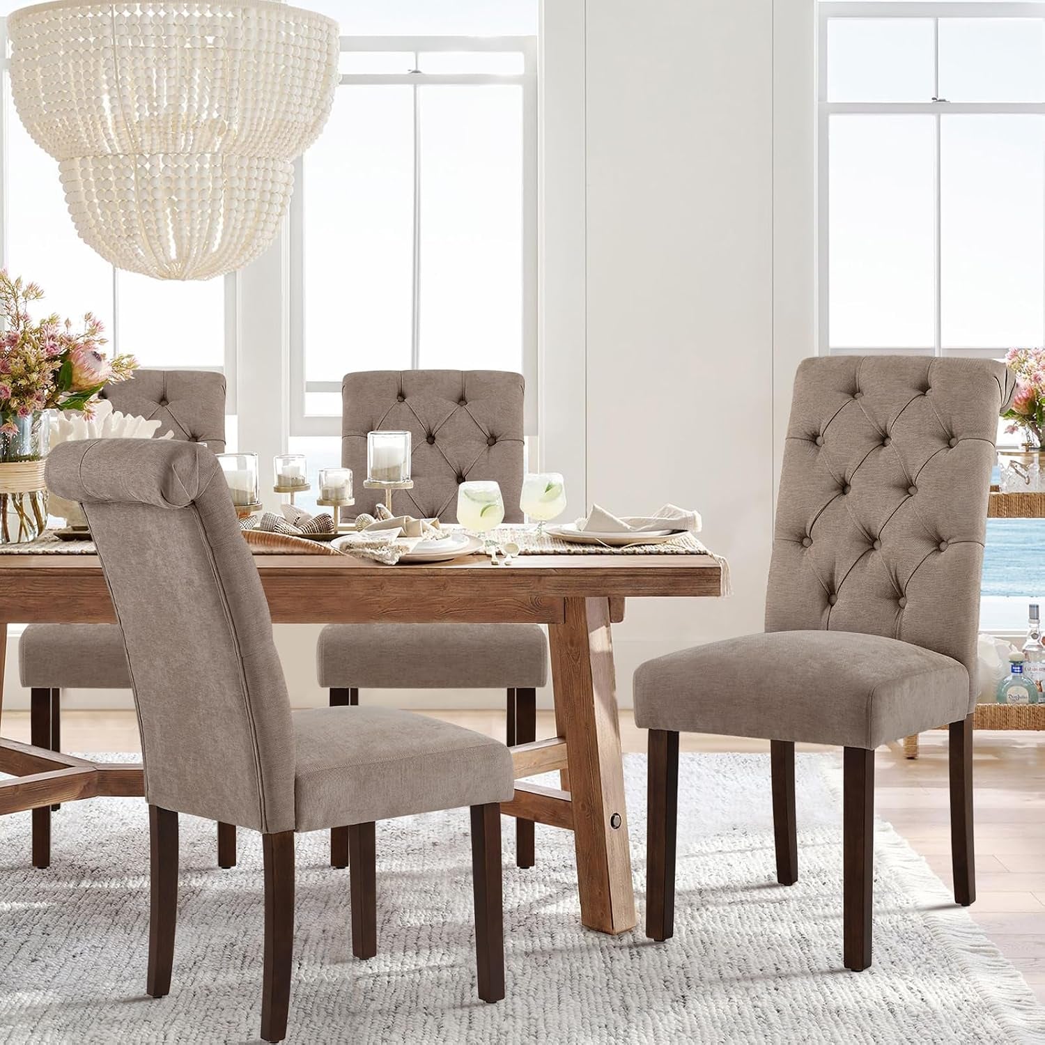 Three taupe Parsons chairs around a rustic dining table with chandelier above in a styled dining room