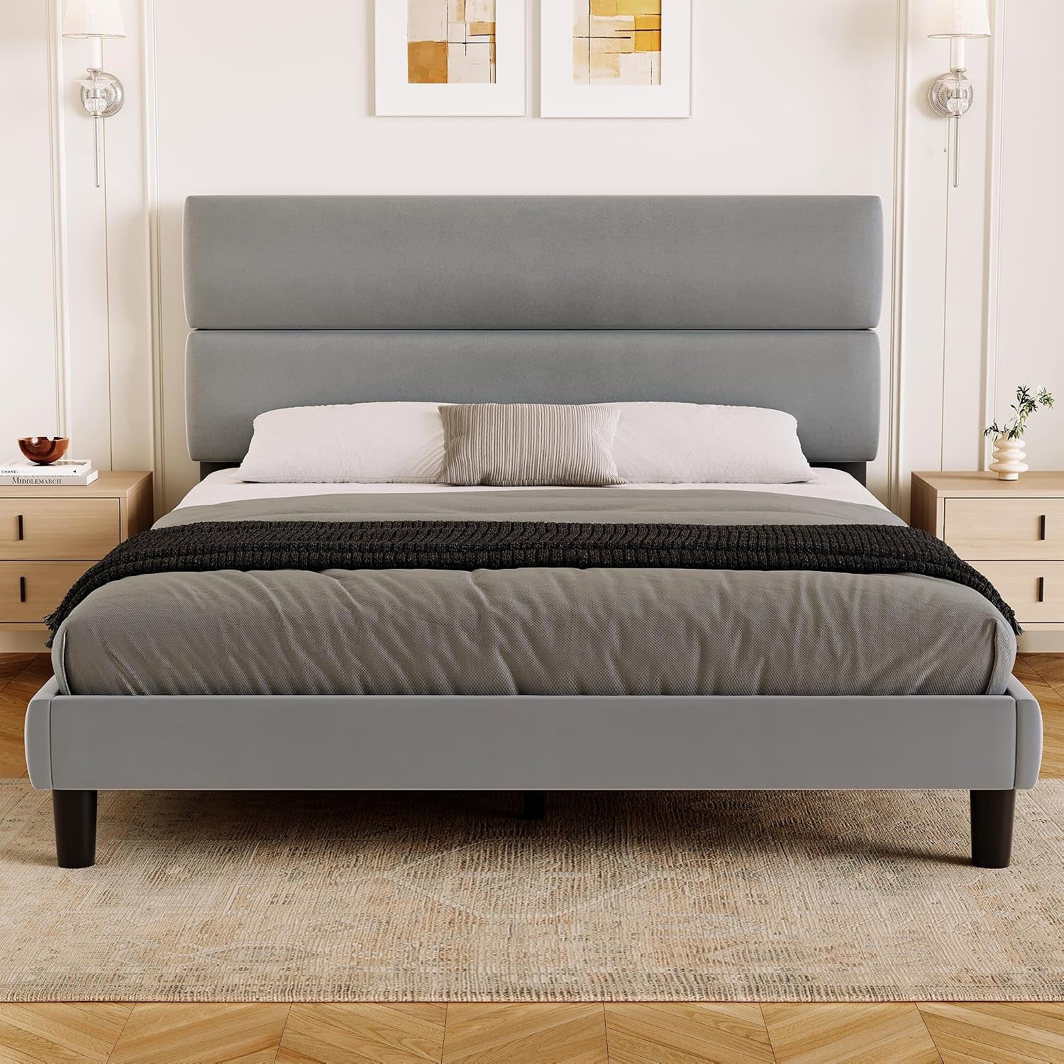 Full front room shot of a gray upholstered bed with a broad two-panel headboard and black legs.