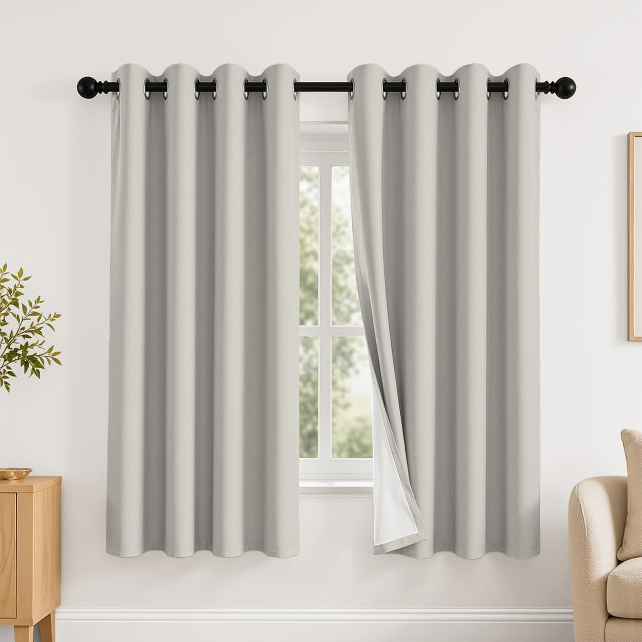 Window dressed with two light gray grommet curtains, right panel slightly pulled to show white backing.