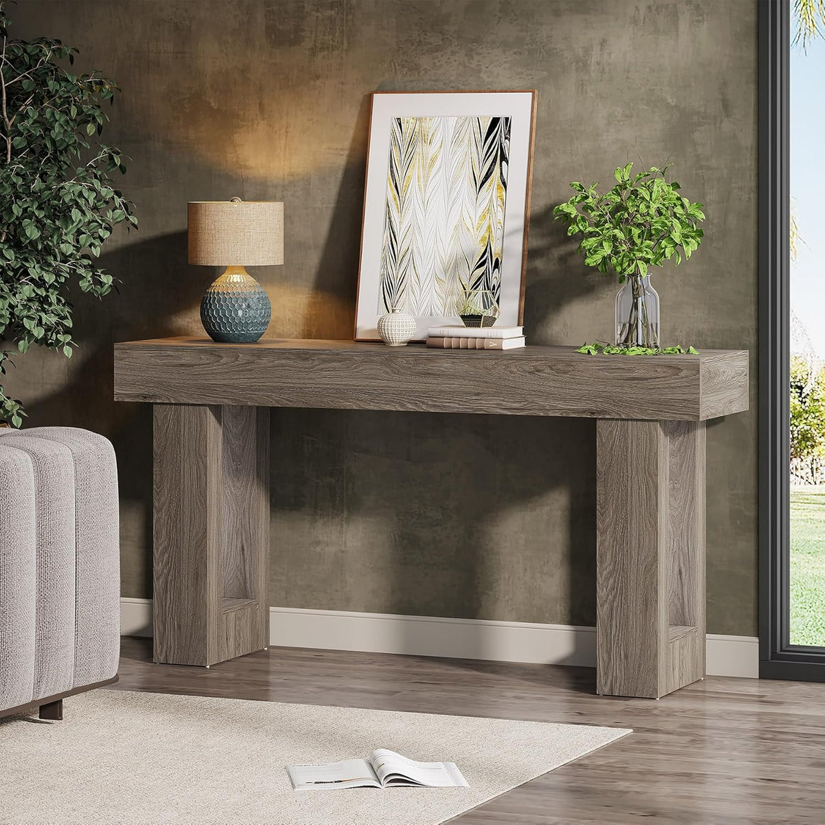 Grey farmhouse console table against a textured wall with framed art propped on top and a table lamp