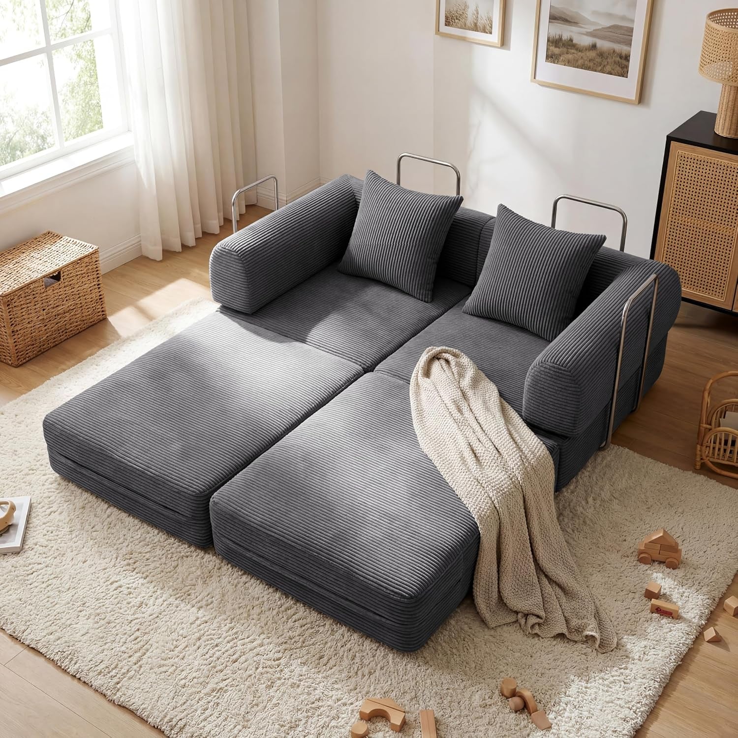 Gray corduroy sofa unfolded into a low bed with two pillows, metal side rails and a knit throw.