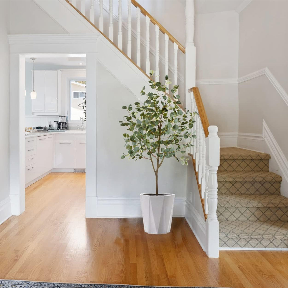 Eucalyptus plant in a white faceted planter tucked at the base of a carpeted staircase.