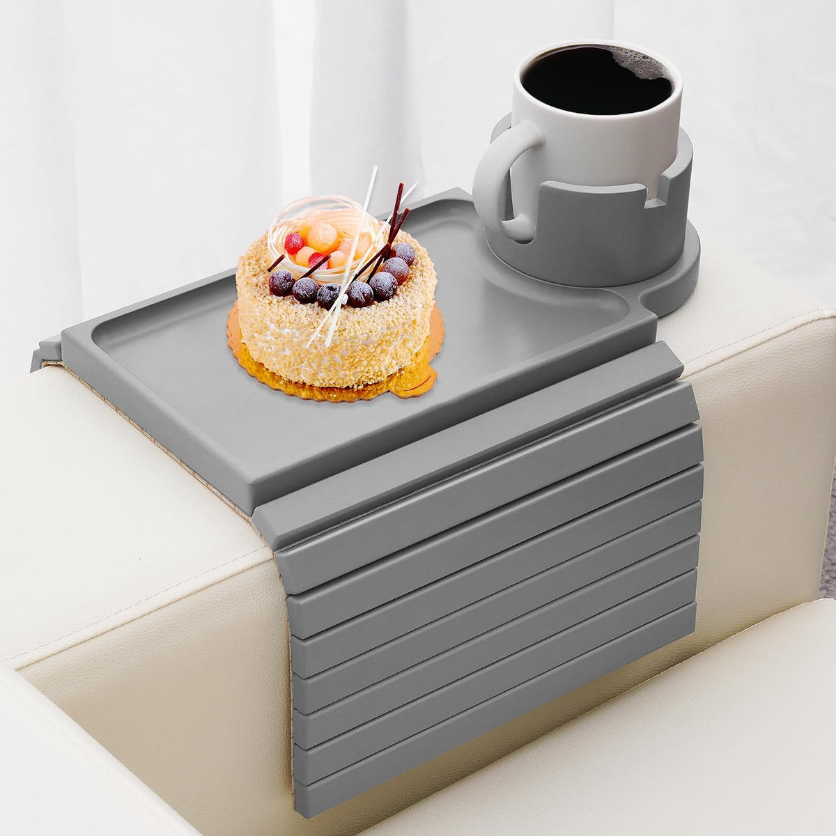 Gray arm tray laid over a sofa arm holding a cake and a mug in the round cup holder.