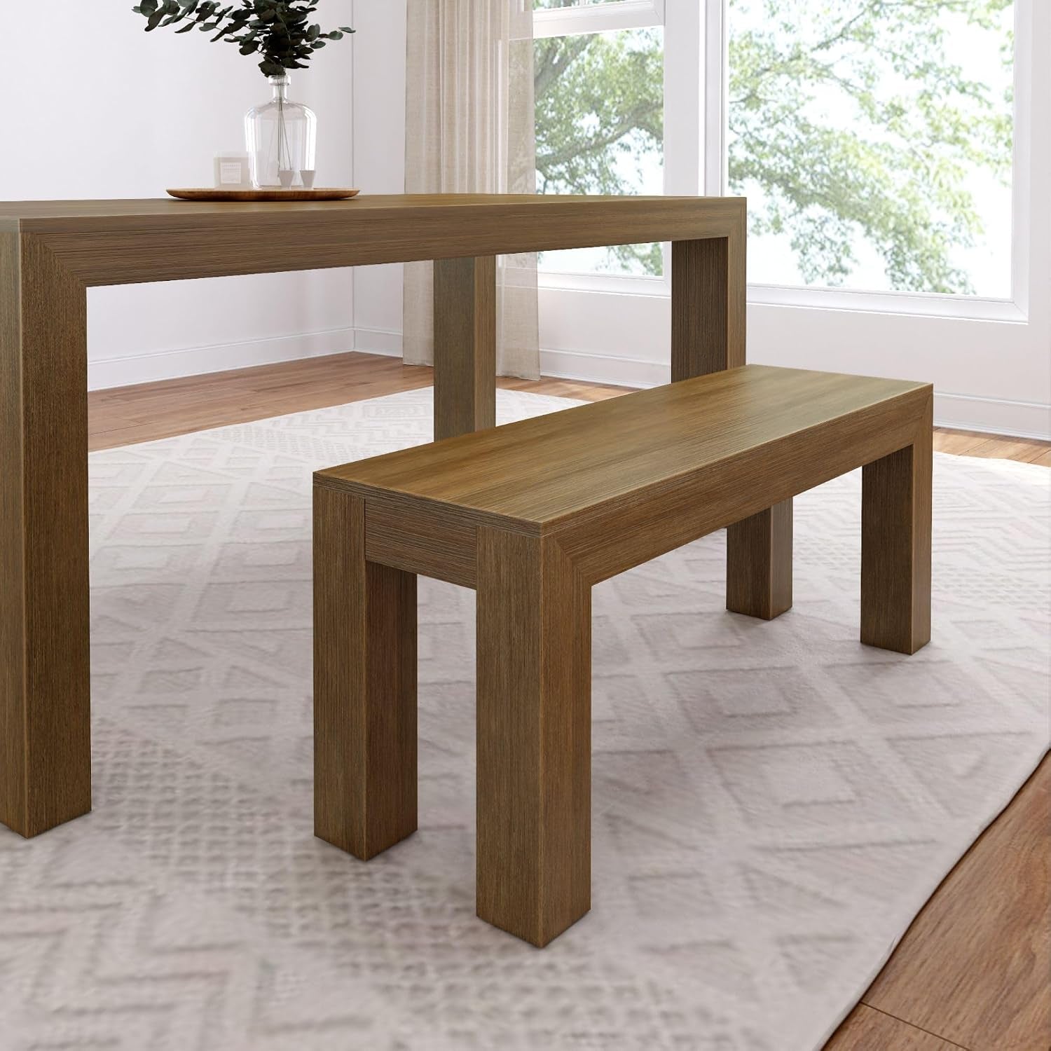 Dining table and bench in a darker wood tone shown in a bright room with a large window.