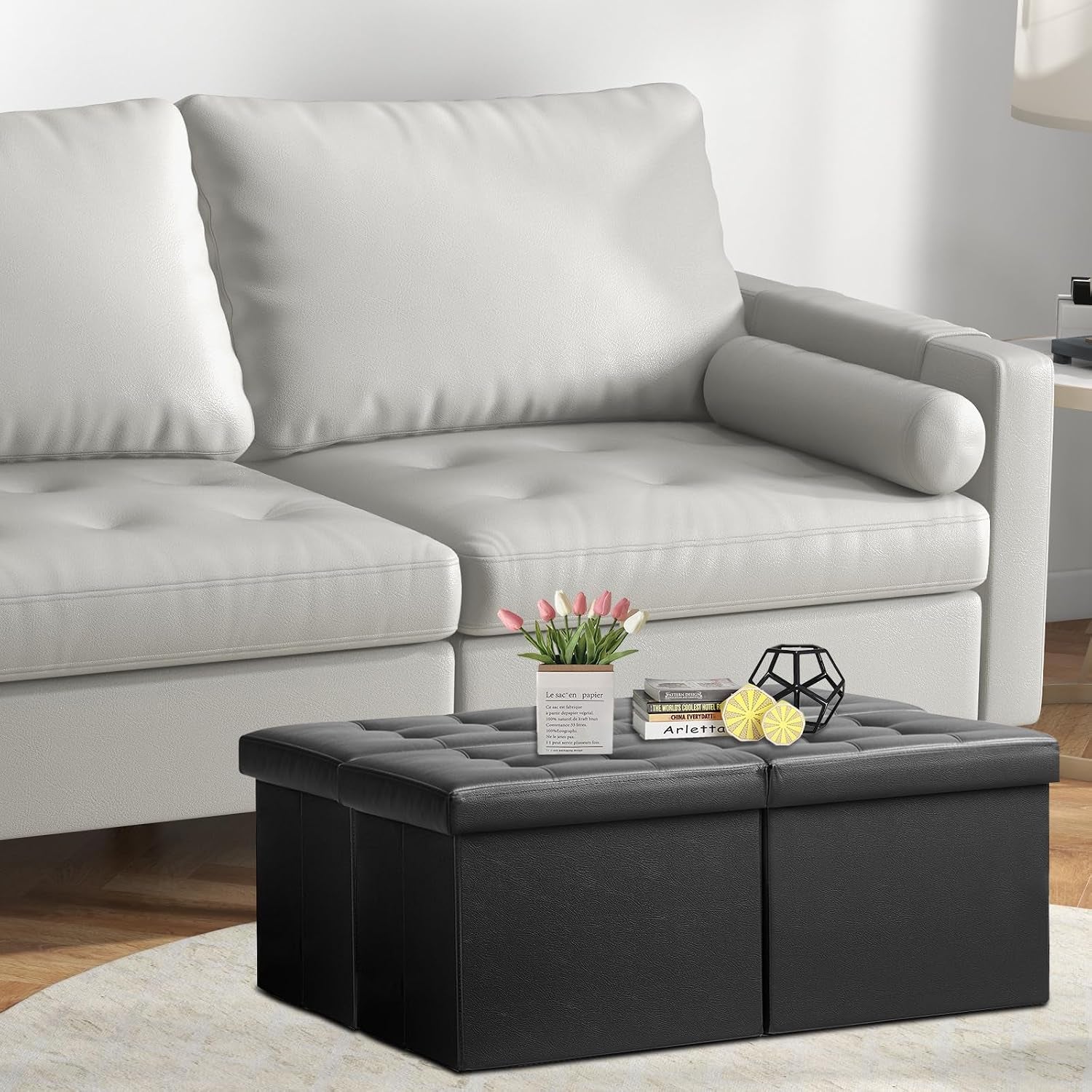 Black leather tufted ottoman used as a small coffee table in front of a light-colored sofa