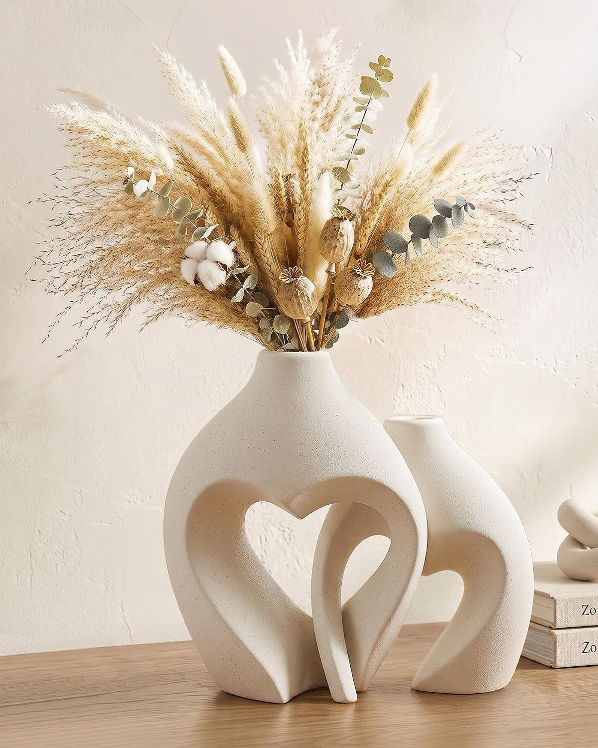 Matte sand-glaze ceramic heart vases set on a wooden table with pampas grass, front angled view
