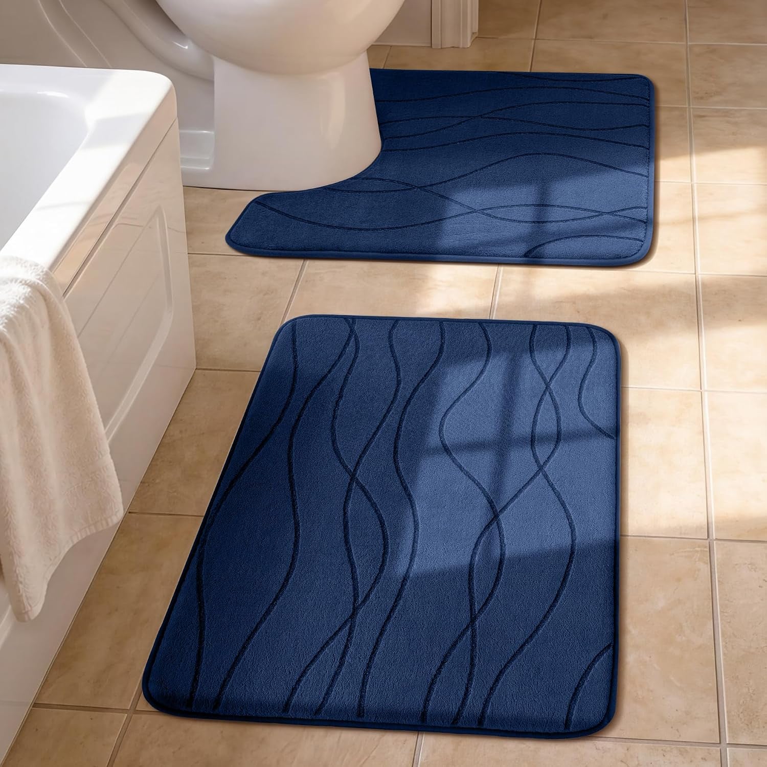 Two navy blue bath mats with wavy stitched pattern placed on beige tile beside a tub and toilet.