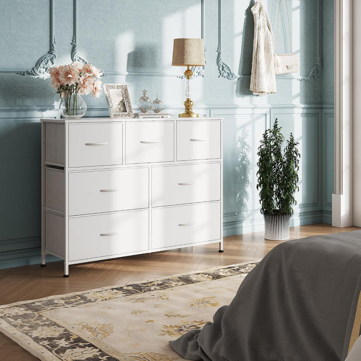 White 7-drawer dresser shown in a sunlit bedroom corner against blue decorative wall.