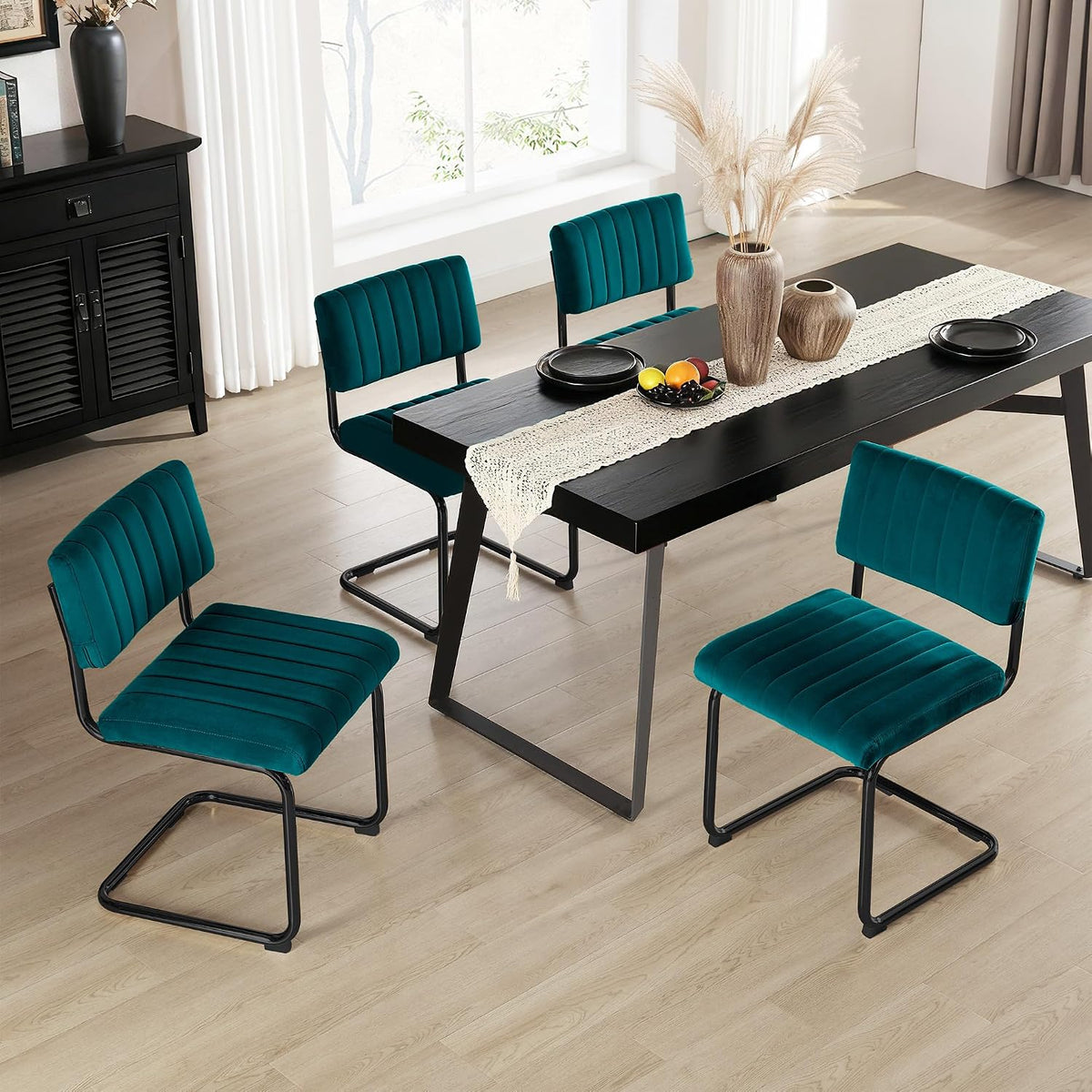 Overhead view of four teal velvet cantilever chairs around a black wood dining table in a bright room