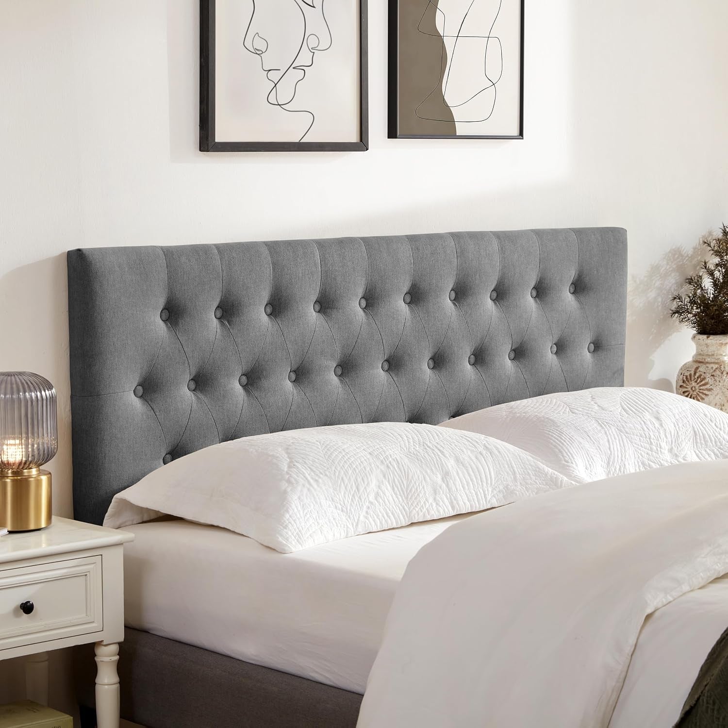 Charcoal gray tufted headboard seen from the side above a dressed bed and bedside table.