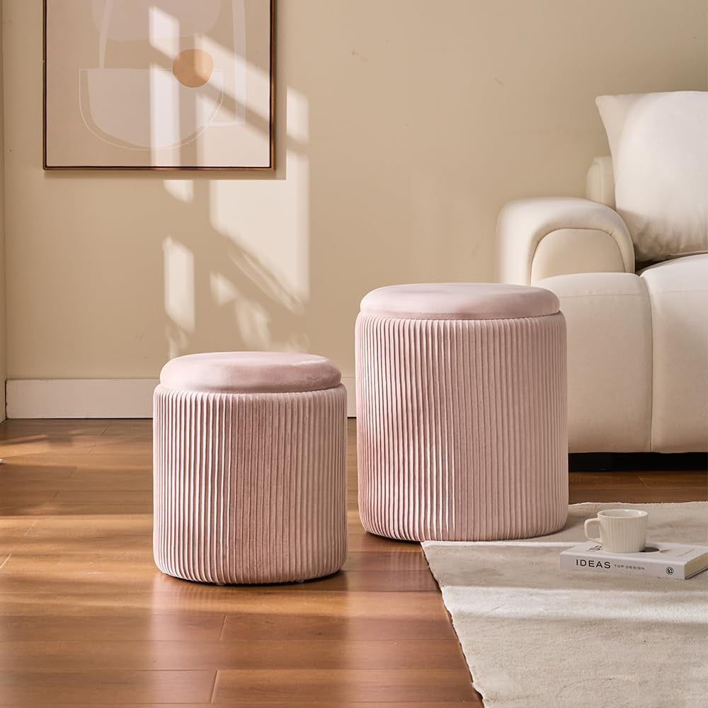 Blush pink round ottoman set beside a sofa in a living room, angled front view with a cup and book nearby