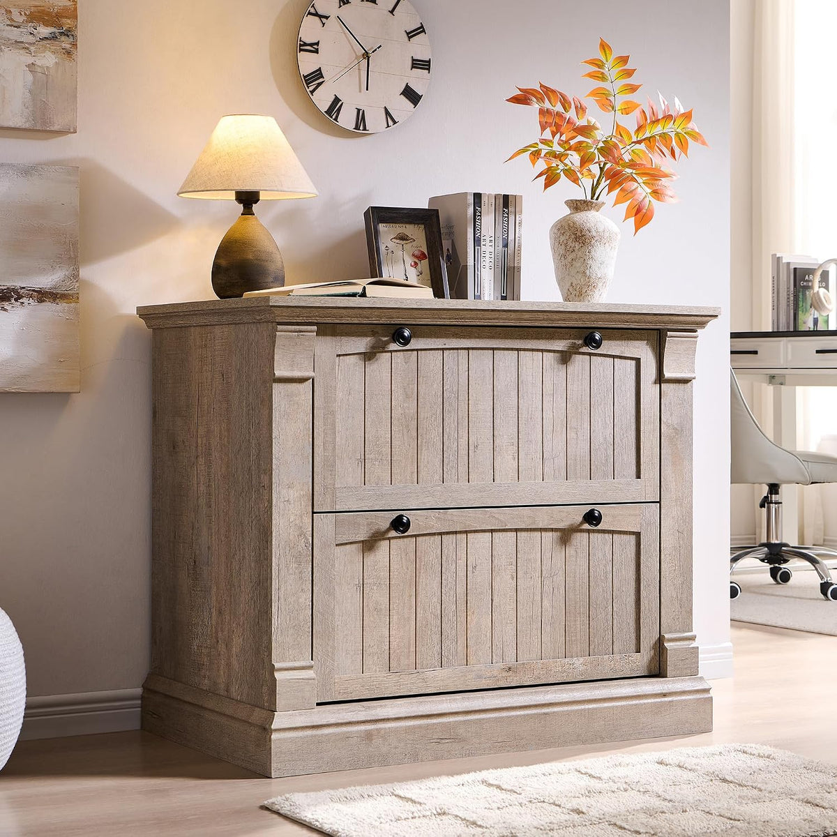 Light gray wood-finish two-drawer file cabinet beside a lamp and books, shown in a bright room.