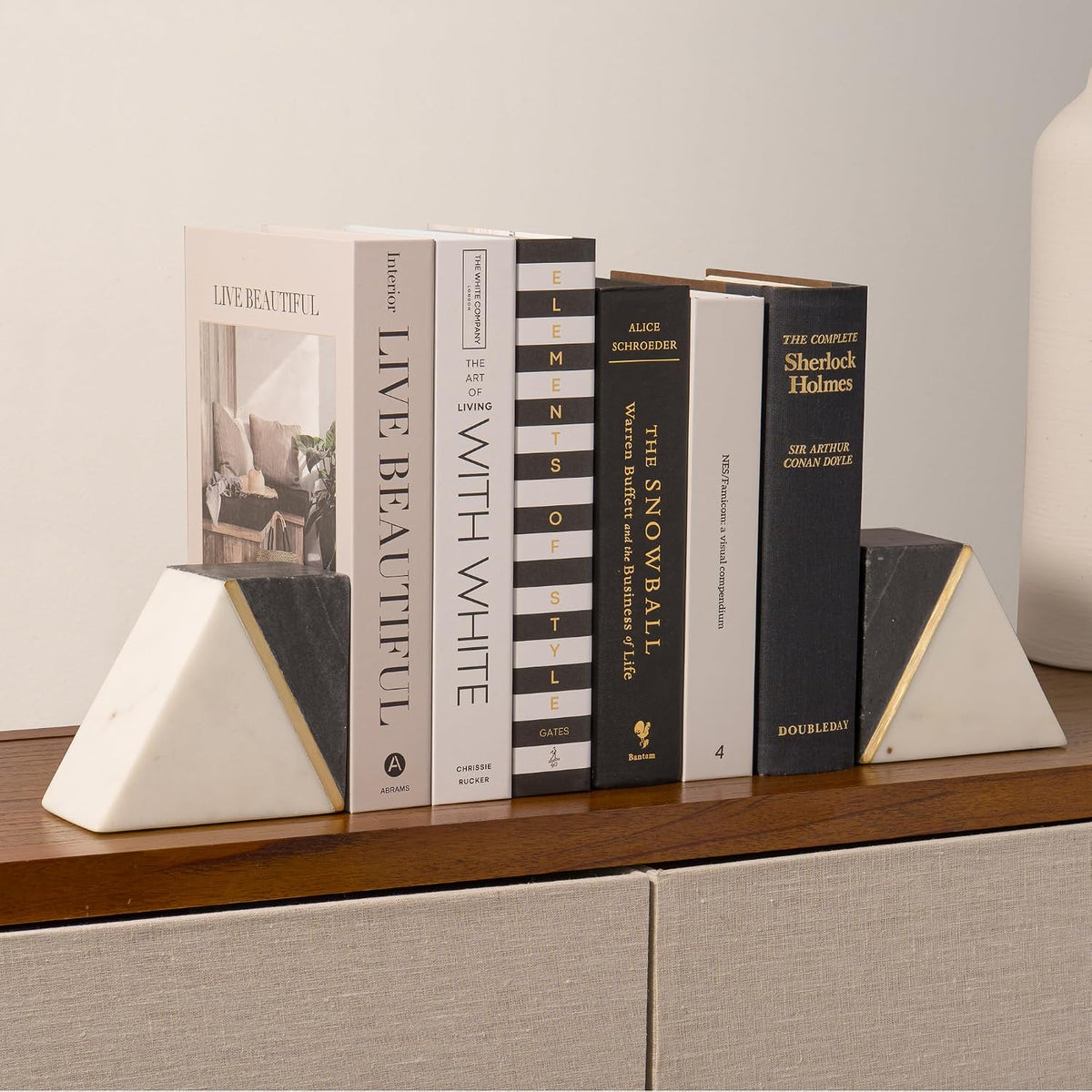 Bookends placed on a wooden console holding a row of books between them against a pale wall
