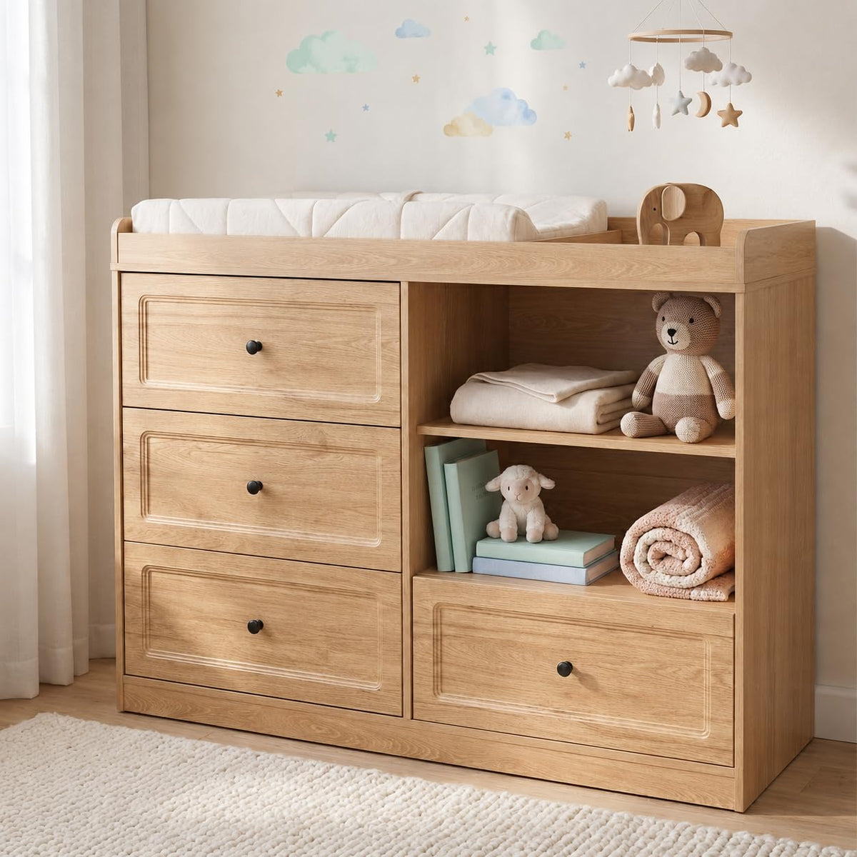 Natural wood changing table with drawers and open shelves styled with toys, blankets, and a mobile in a nursery.