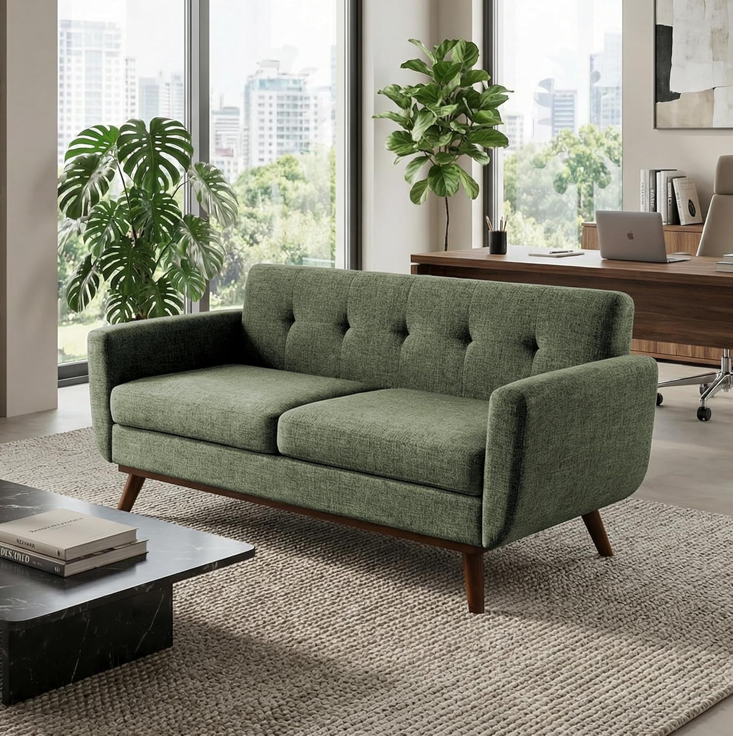 Green mid-century loveseat placed on a rug in a bright room with plants and a desk behind it.