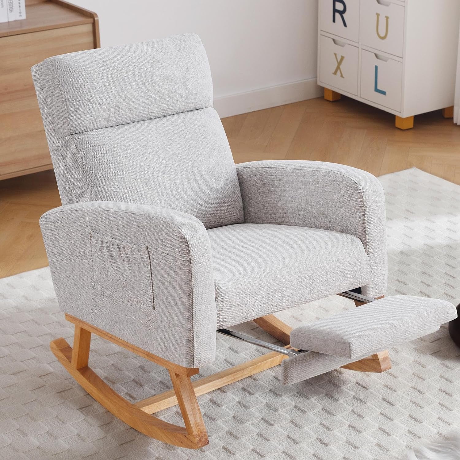 Light gray upholstered glider rocker with tucked arm pocket and footrest partially extended