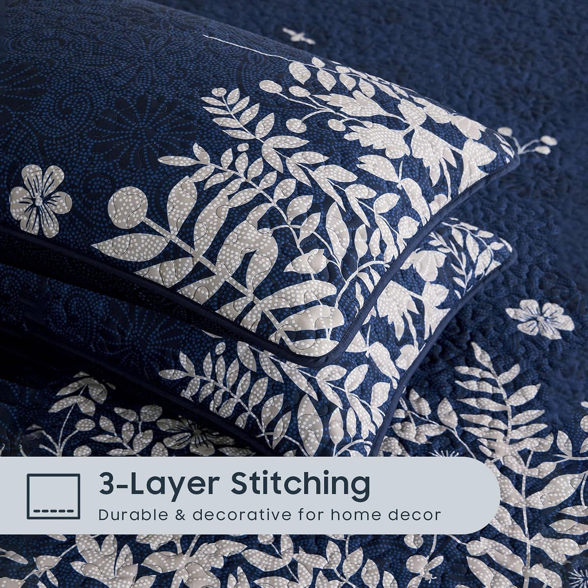 Close-up of two navy pillow shams showing white floral print, detailed quilting and piped edges