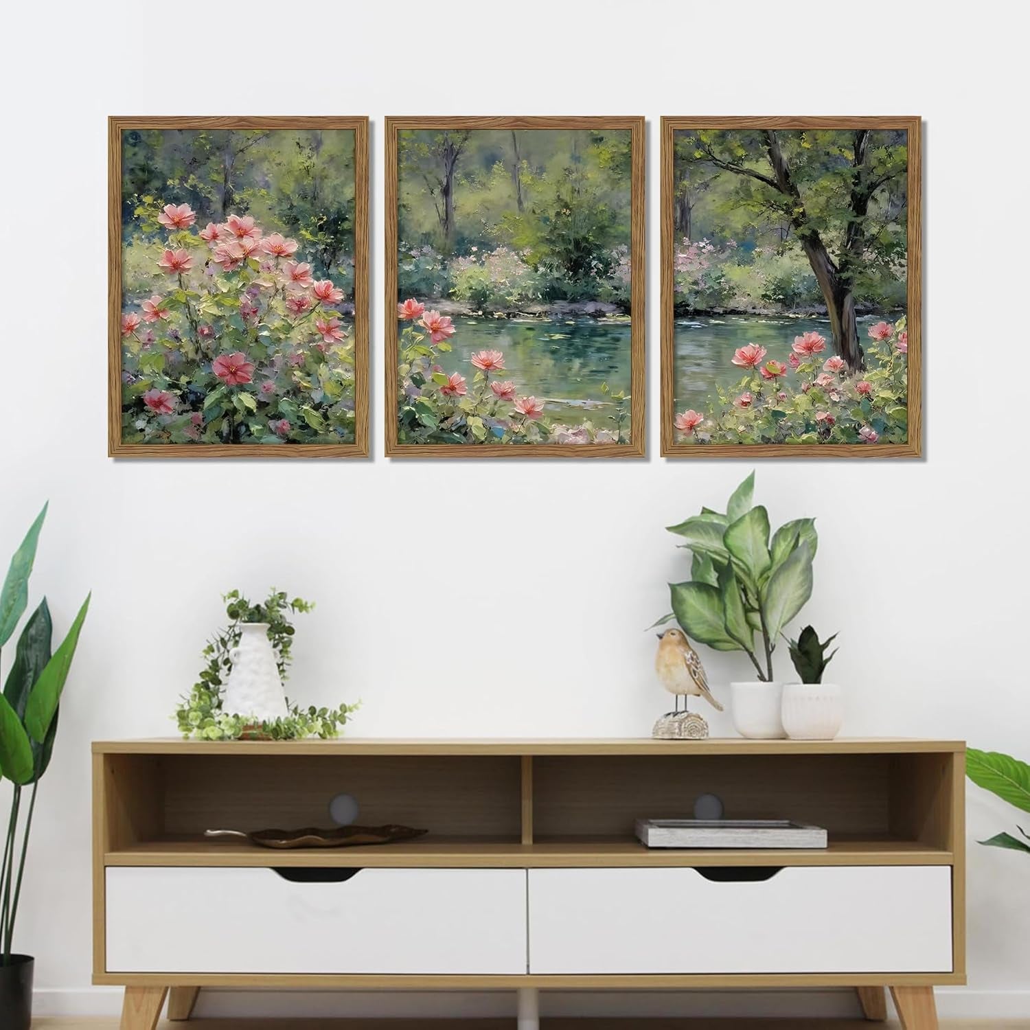 Three wood-framed floral landscape canvases hung above a low console table with plants and decorative accents.