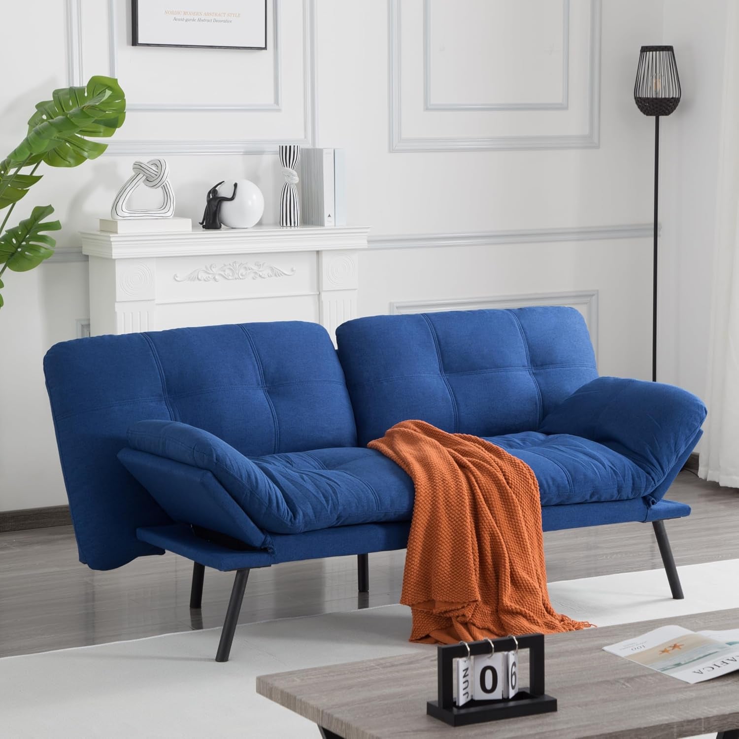 Blue convertible futon with folded armrests and orange throw draped across seat in minimalist living room.