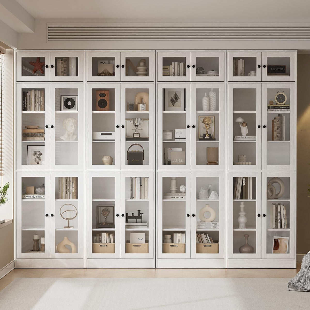 Full wall of tall white bookcases with glass upper doors and styled shelves in a bright room.