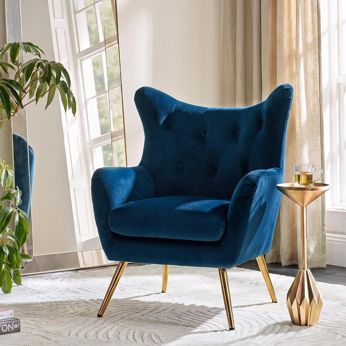 Close three-quarter view of navy velvet wingback chair showing button-tufted back, padded arms and gold-tone legs next to a s
