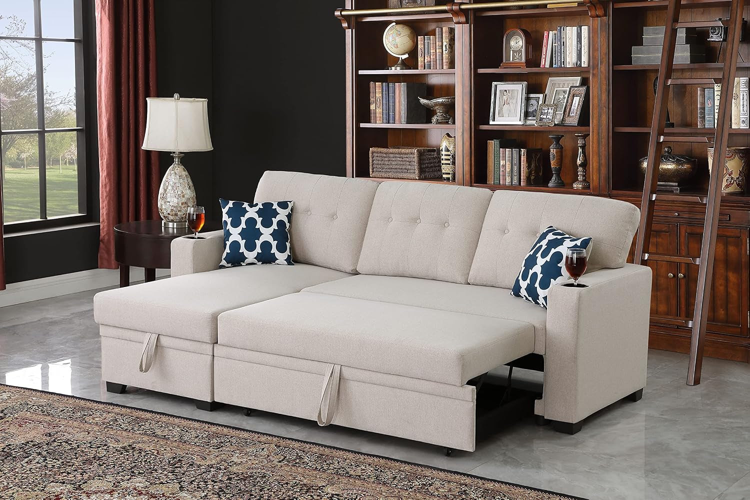 Beige L-shaped sectional with chaise and pulled-out sleeper, tufted back, two blue patterned pillows, drinks on each arm in